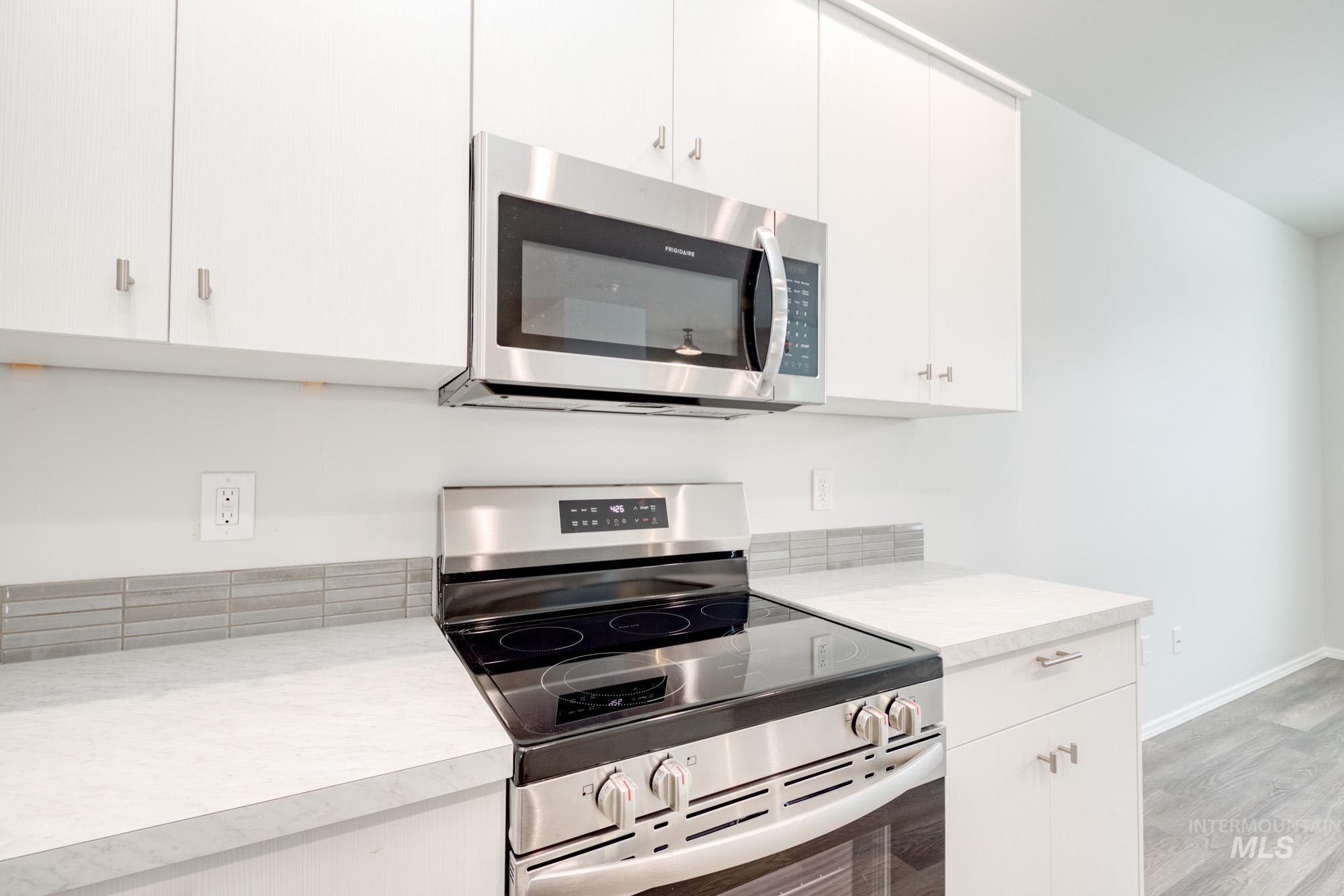 Kitchen with appliances with stainless steel finishes, white cabinets, light countertops, and light wood finished floors
