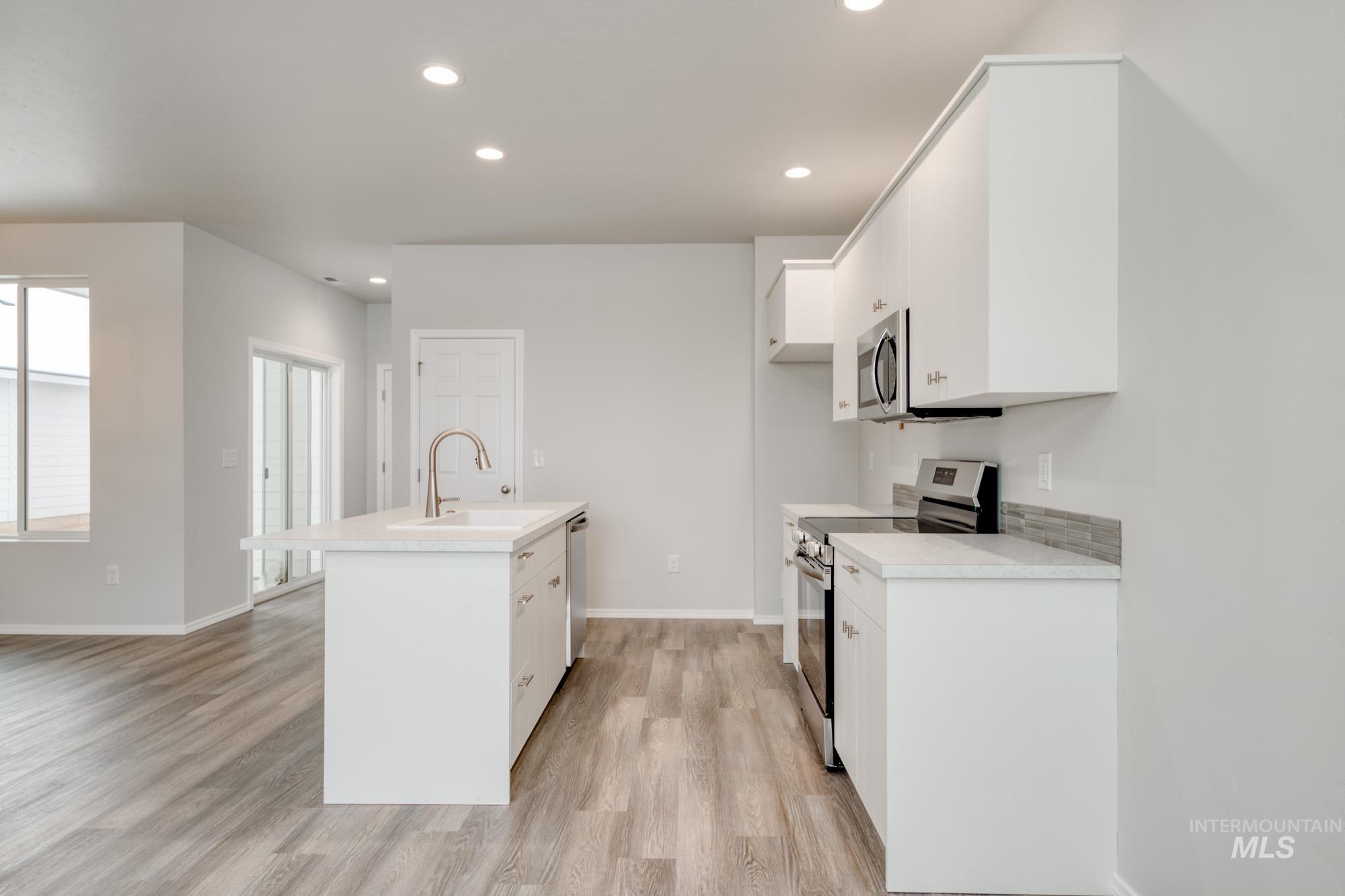 Kitchen featuring stainless steel appliances, light countertops, recessed lighting, white cabinets, and a center island with sink