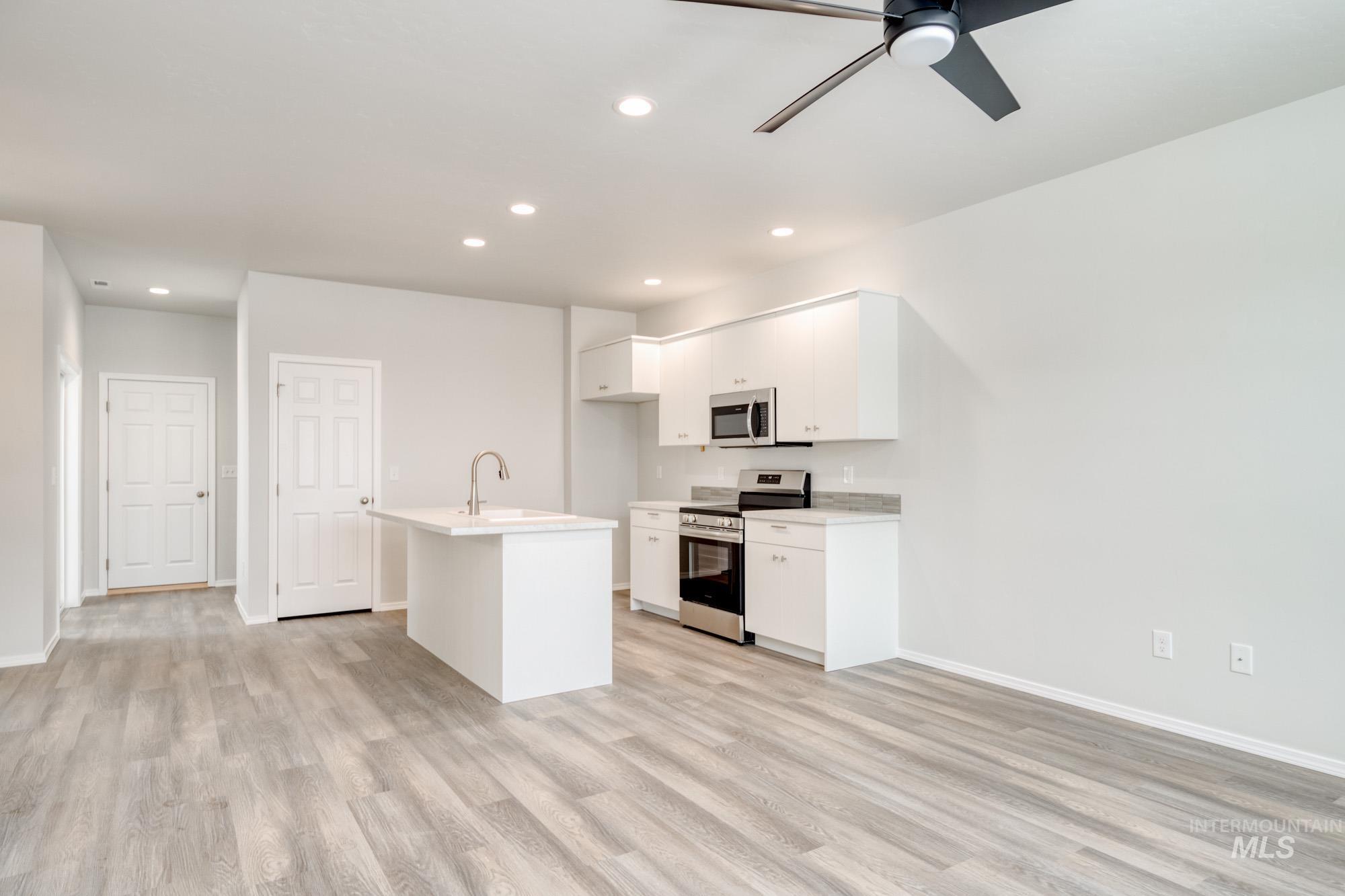 Kitchen featuring appliances with stainless steel finishes, a kitchen island with sink, white cabinets, light wood finished floors, and recessed lighting