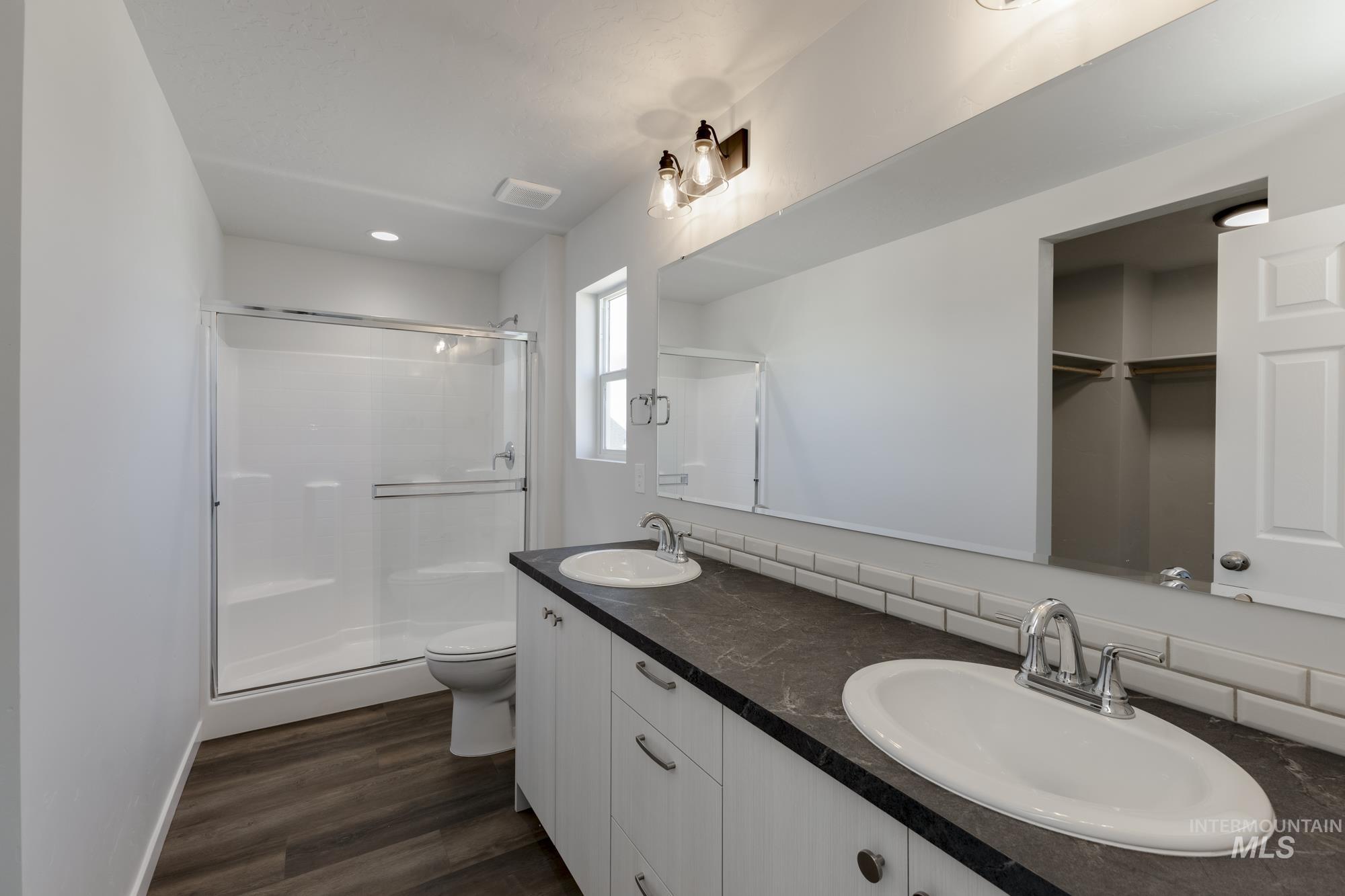 Bathroom featuring double vanity, a stall shower, dark wood finished floors, a walk in closet, and recessed lighting