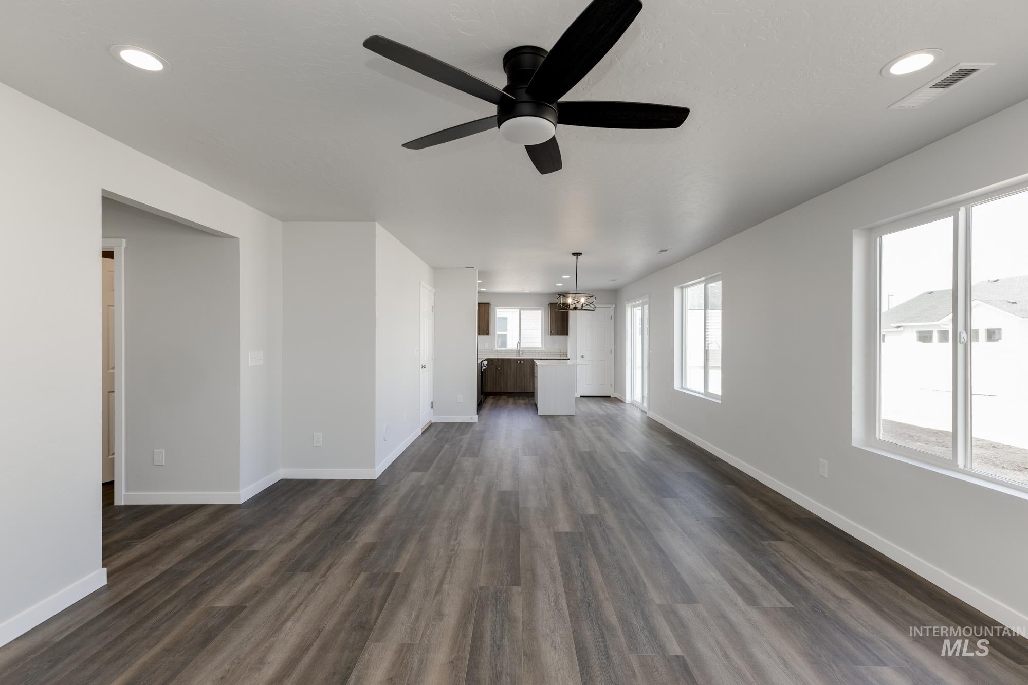 Unfurnished living room featuring recessed lighting, dark wood-style flooring, a chandelier, and ceiling fan