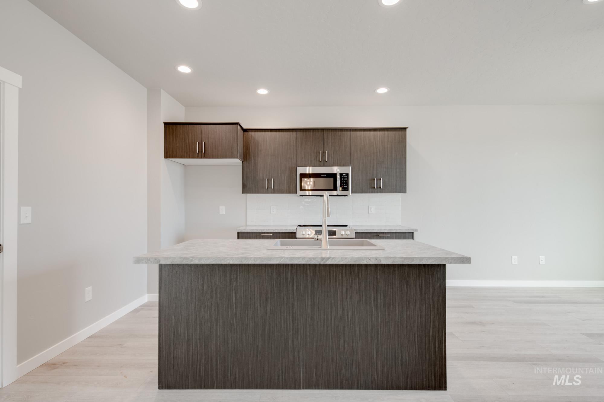 Kitchen featuring dark brown cabinets, recessed lighting, a center island with sink, stainless steel microwave, and light wood finished floors