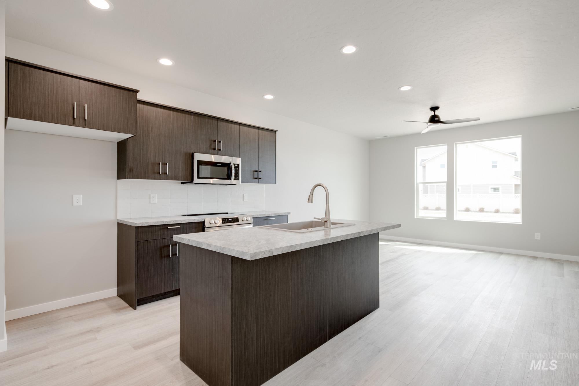 Kitchen with dark brown cabinetry, light countertops, a kitchen island with sink, stainless steel appliances, and recessed lighting