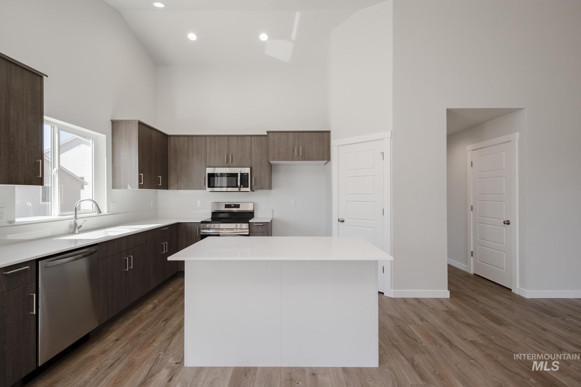 Kitchen with modern cabinets, a towering ceiling, stainless steel appliances, light wood-style floors, and dark brown cabinets