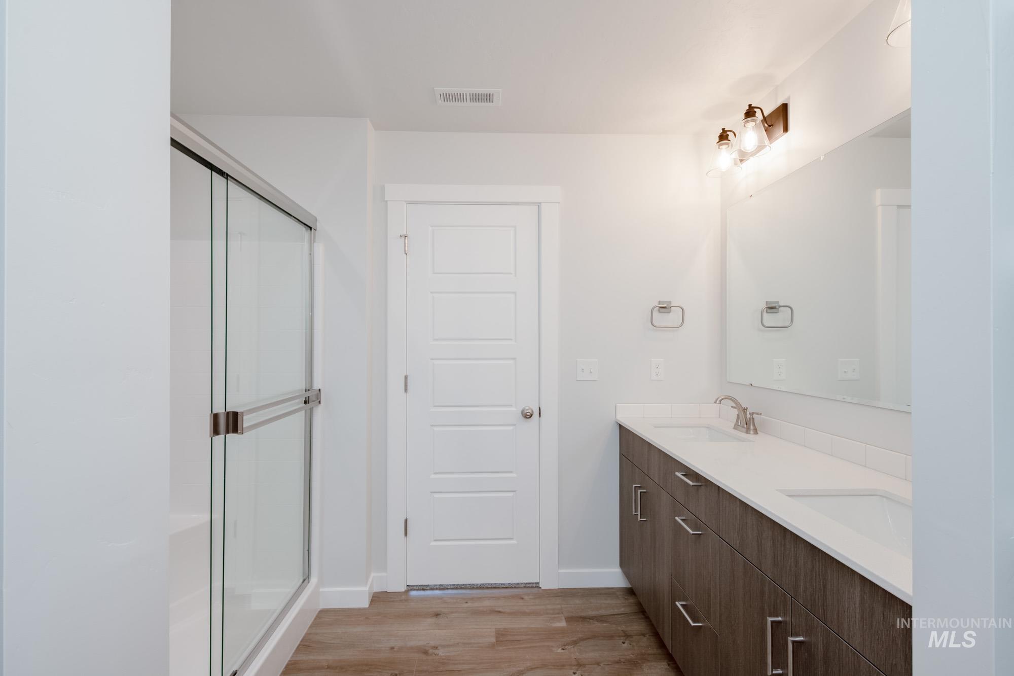 Full bathroom with light wood-type flooring, double vanity, and a stall shower