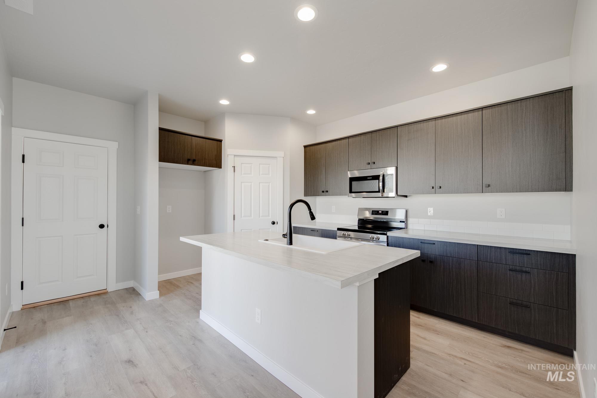 Kitchen with light countertops, appliances with stainless steel finishes, recessed lighting, a kitchen island with sink, and light wood-style flooring