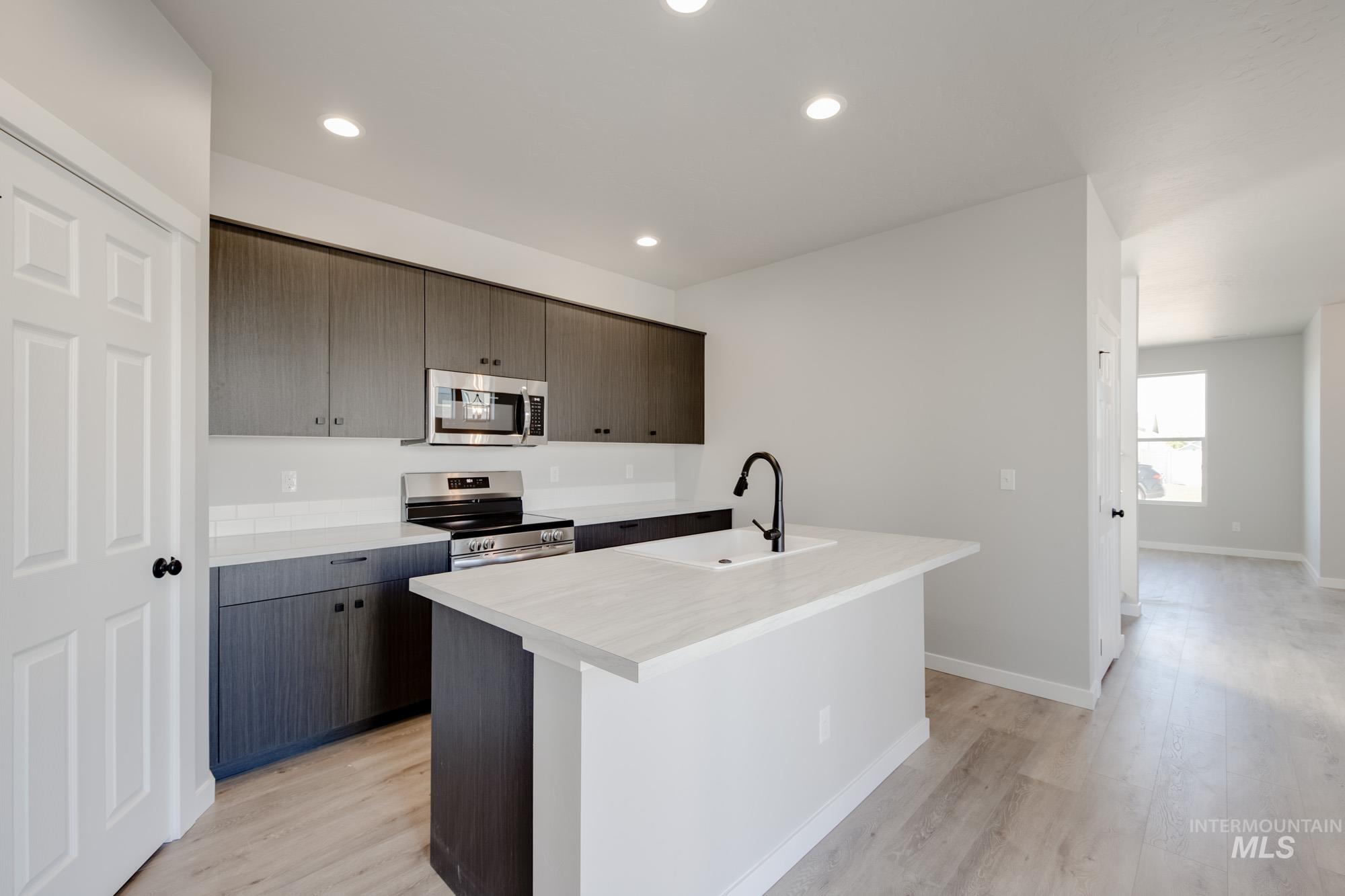 Kitchen with light countertops, appliances with stainless steel finishes, a center island with sink, light wood-style flooring, and dark brown cabinets