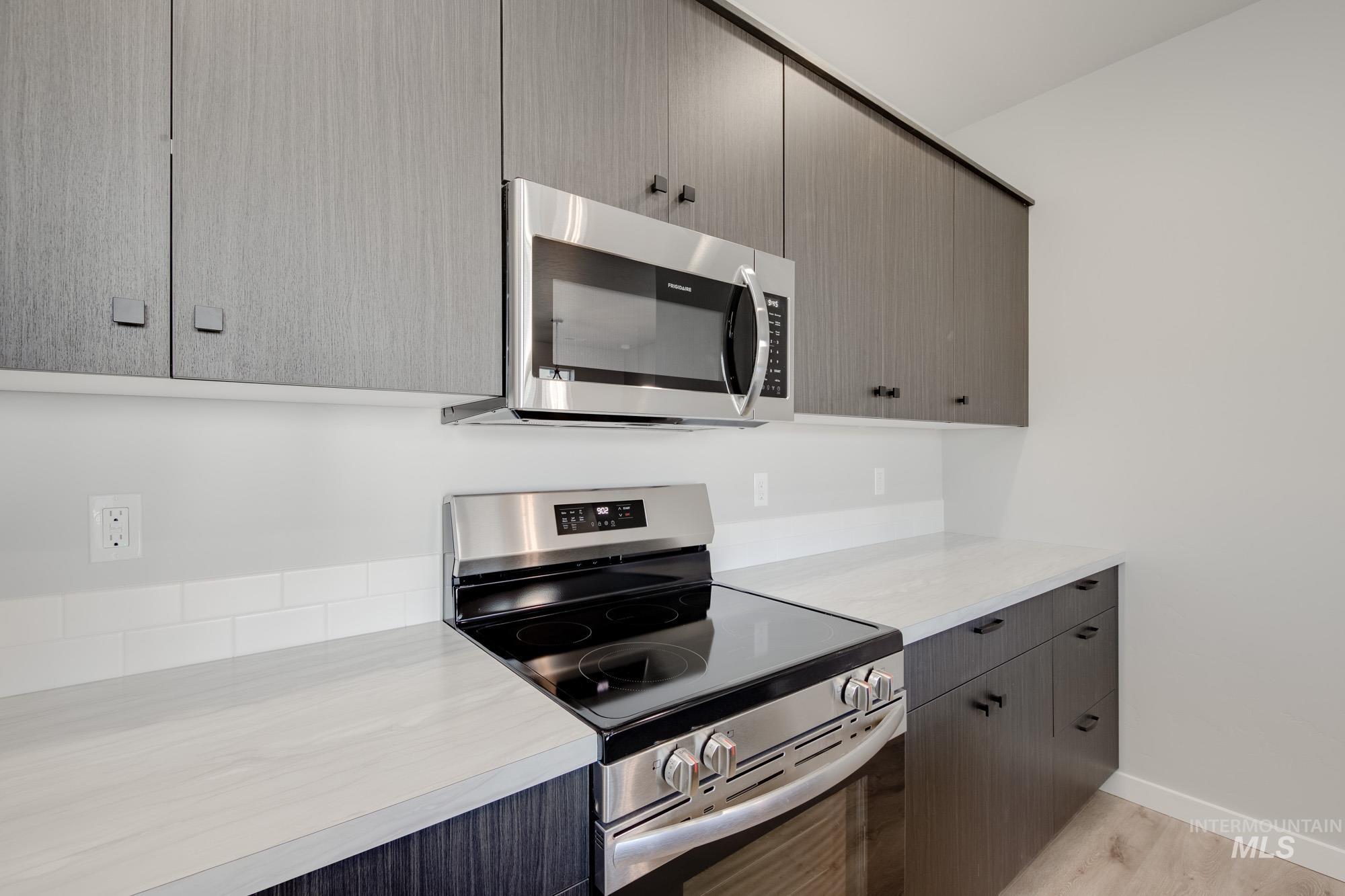 Kitchen with appliances with stainless steel finishes, light countertops, gray cabinetry, light wood finished floors, and modern cabinets