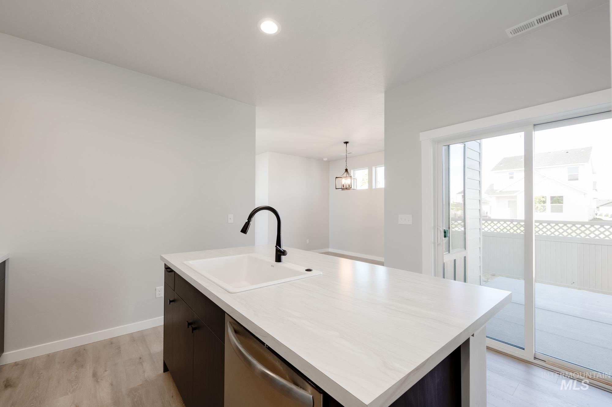 Kitchen featuring light wood-type flooring, light countertops, an island with sink, stainless steel dishwasher, and decorative light fixtures