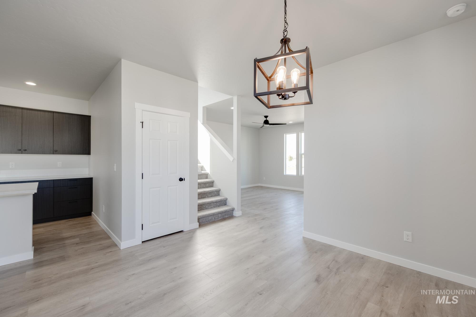 Unfurnished dining area featuring a chandelier, light wood-style floors, ceiling fan, and stairs