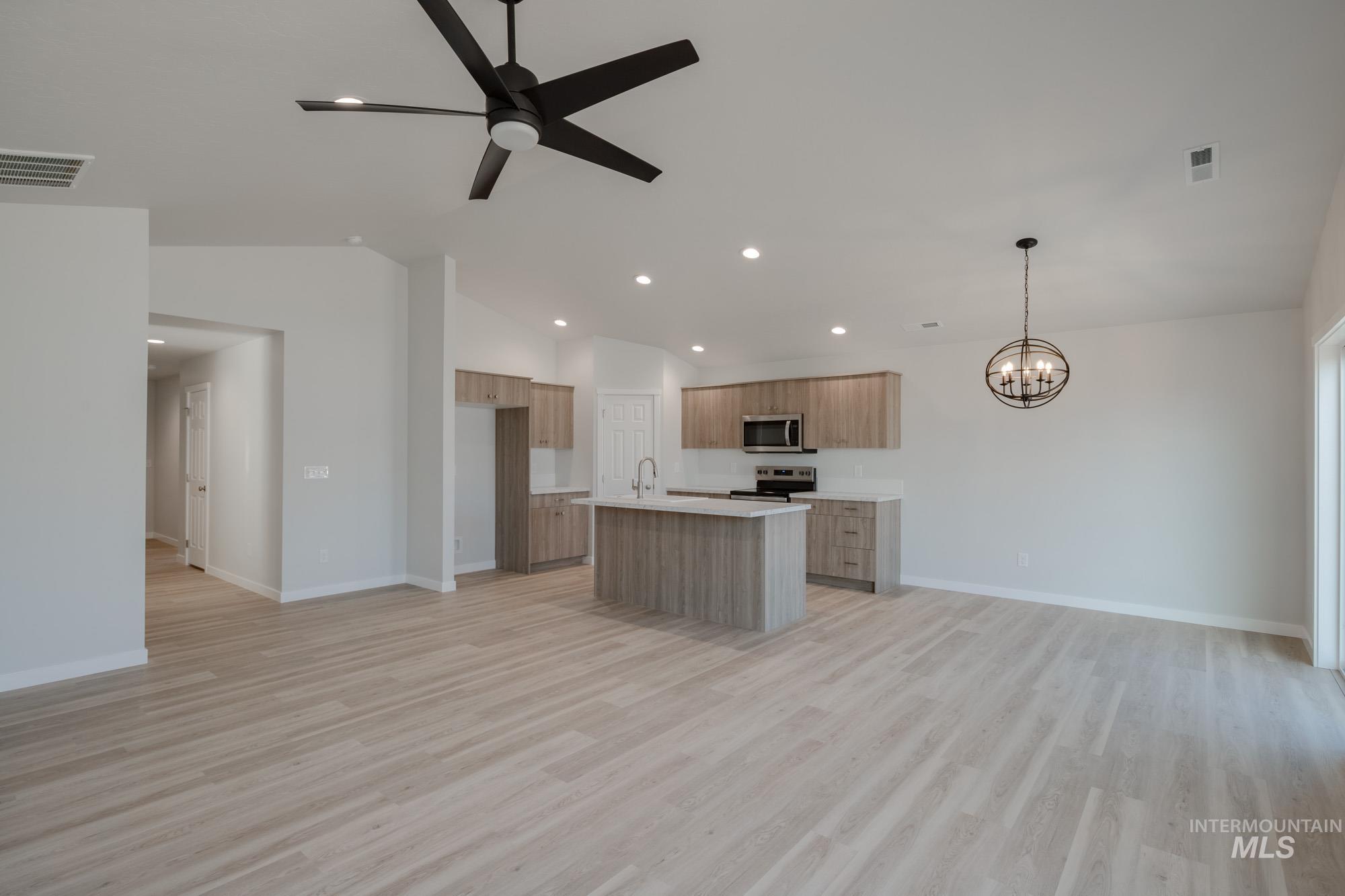 Kitchen featuring open floor plan, light countertops, an island with sink, vaulted ceiling, and light wood finished floors