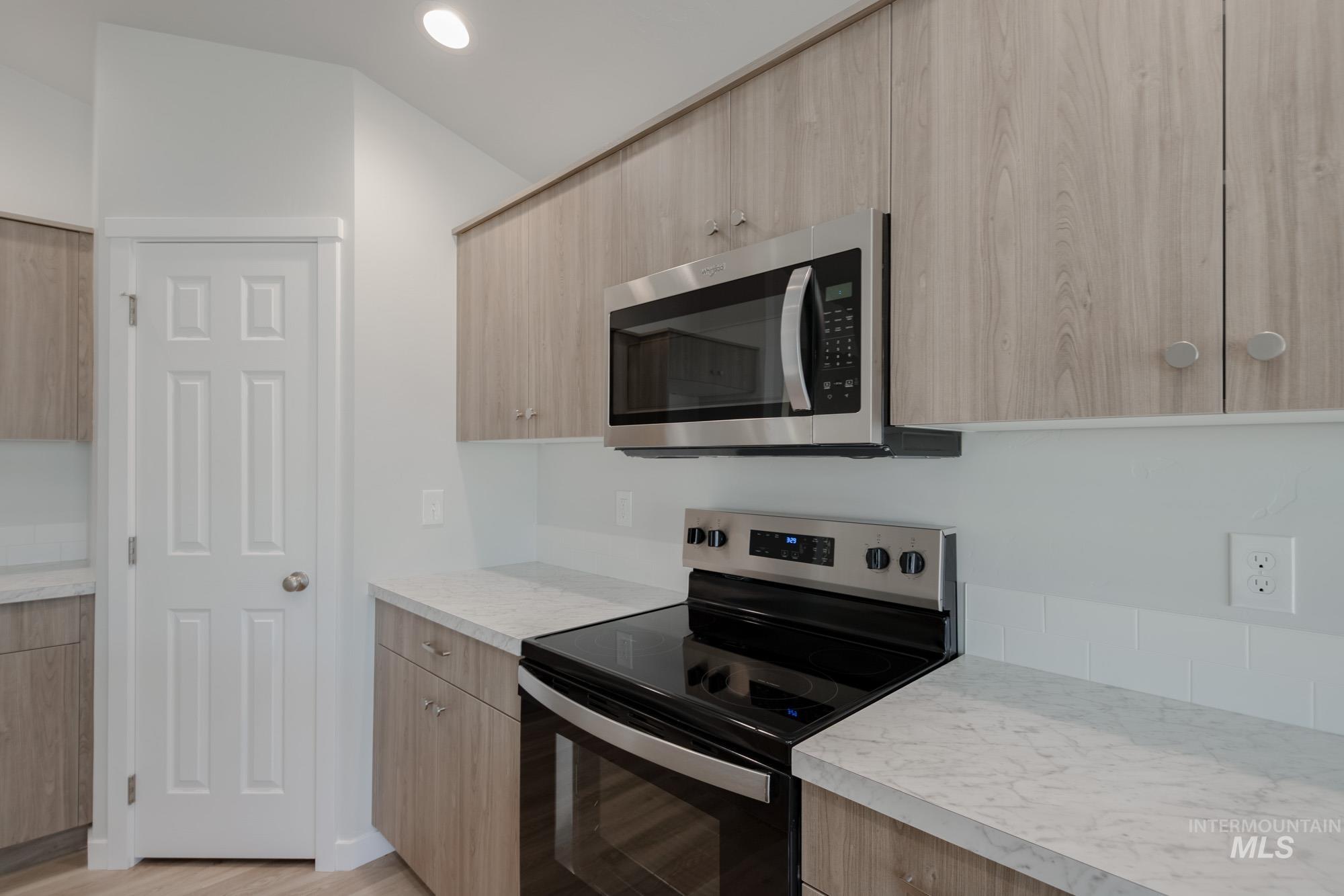 Kitchen with appliances with stainless steel finishes, light countertops, light wood-type flooring, light brown cabinets, and modern cabinets