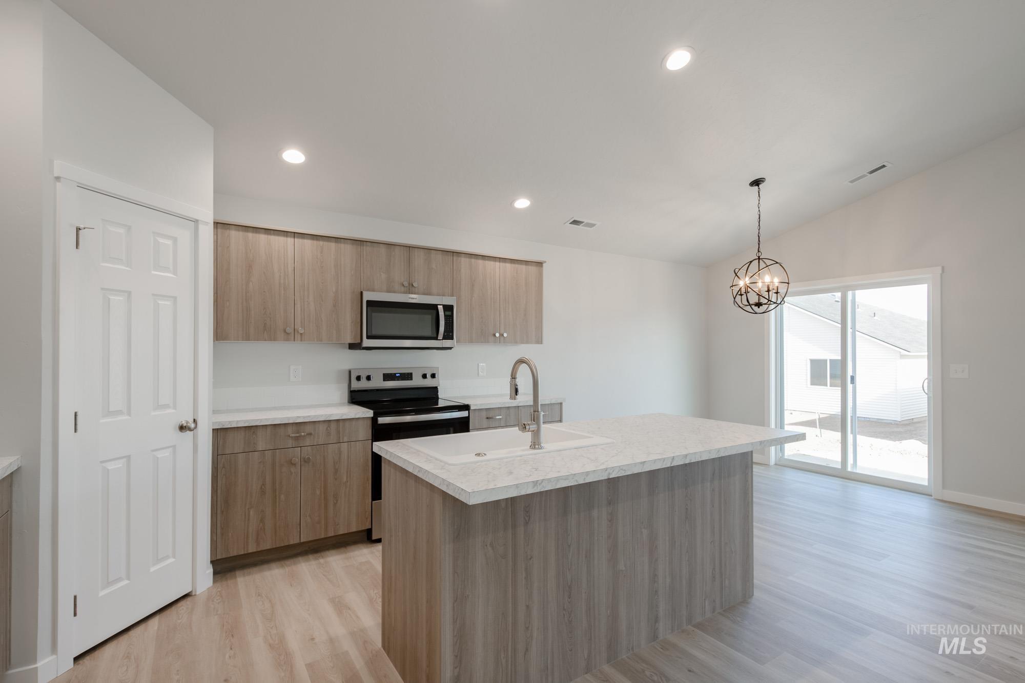 Kitchen featuring light countertops, stainless steel appliances, light wood-style flooring, a kitchen island with sink, and decorative light fixtures