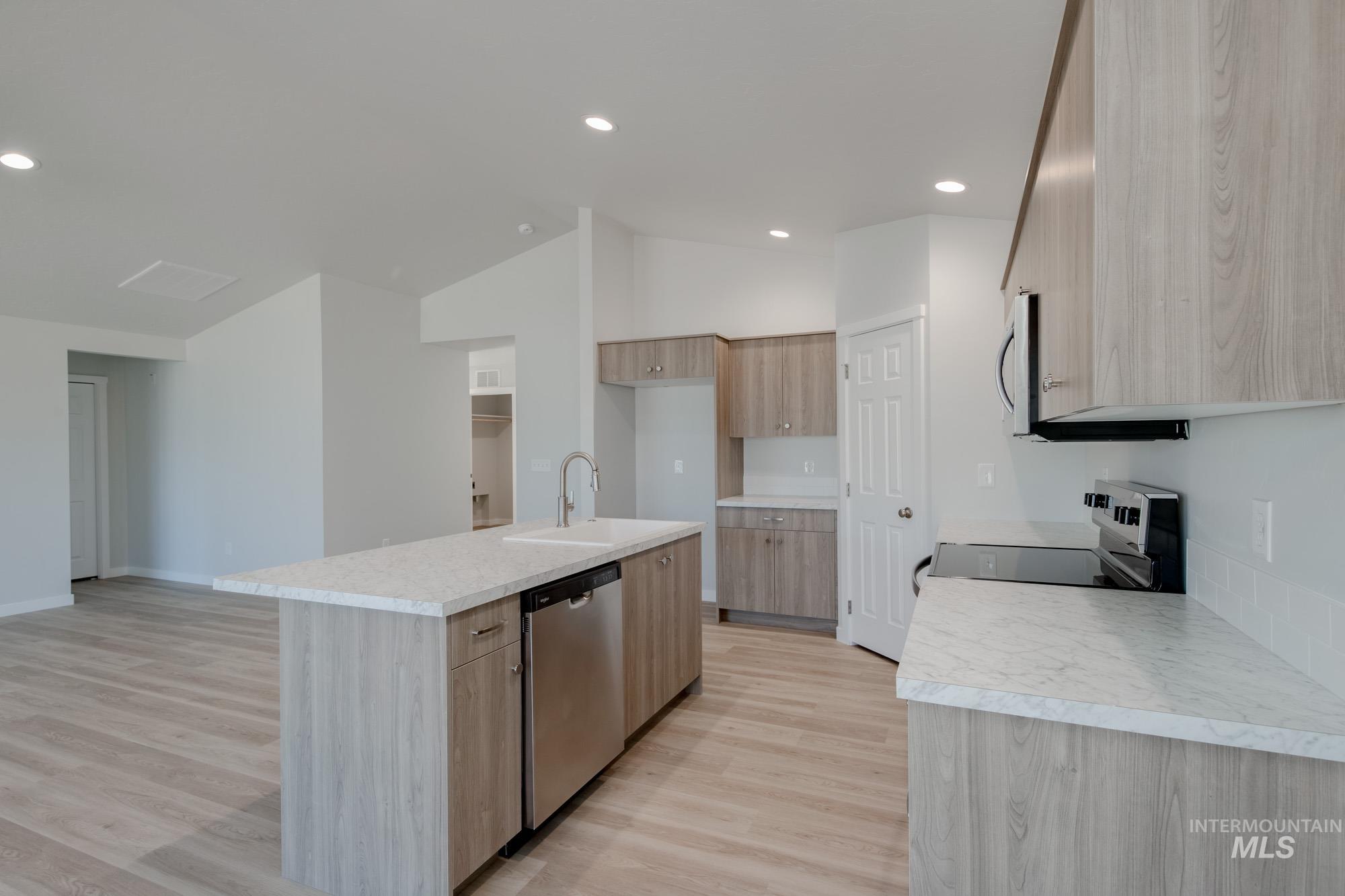 Kitchen with light countertops, stainless steel appliances, light wood-type flooring, recessed lighting, and a center island with sink