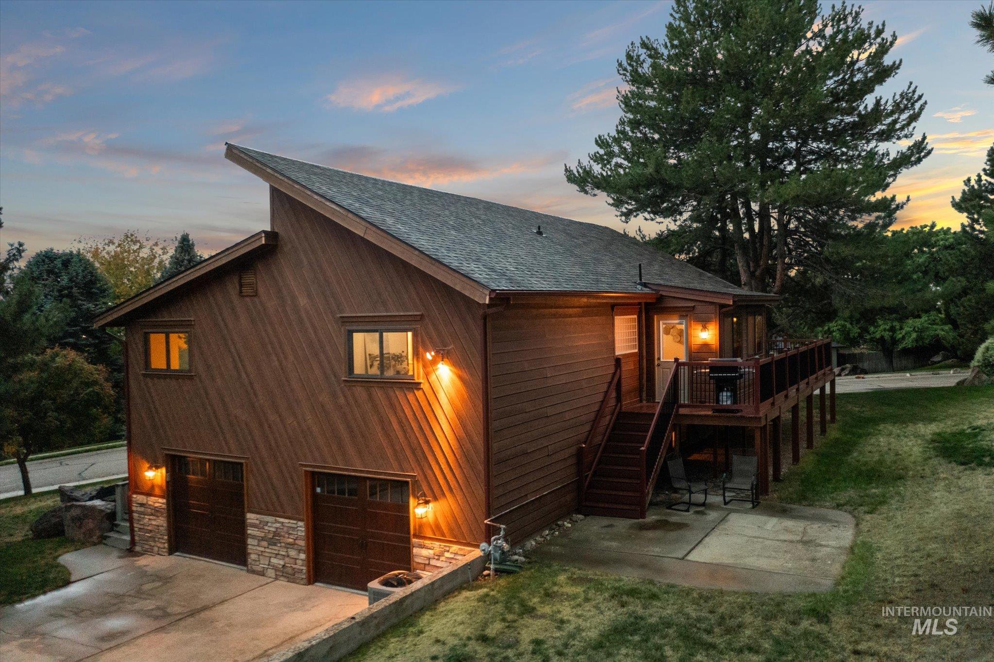 Property exterior at dusk with stairway, a shingled roof, a patio, a deck, and a lawn
