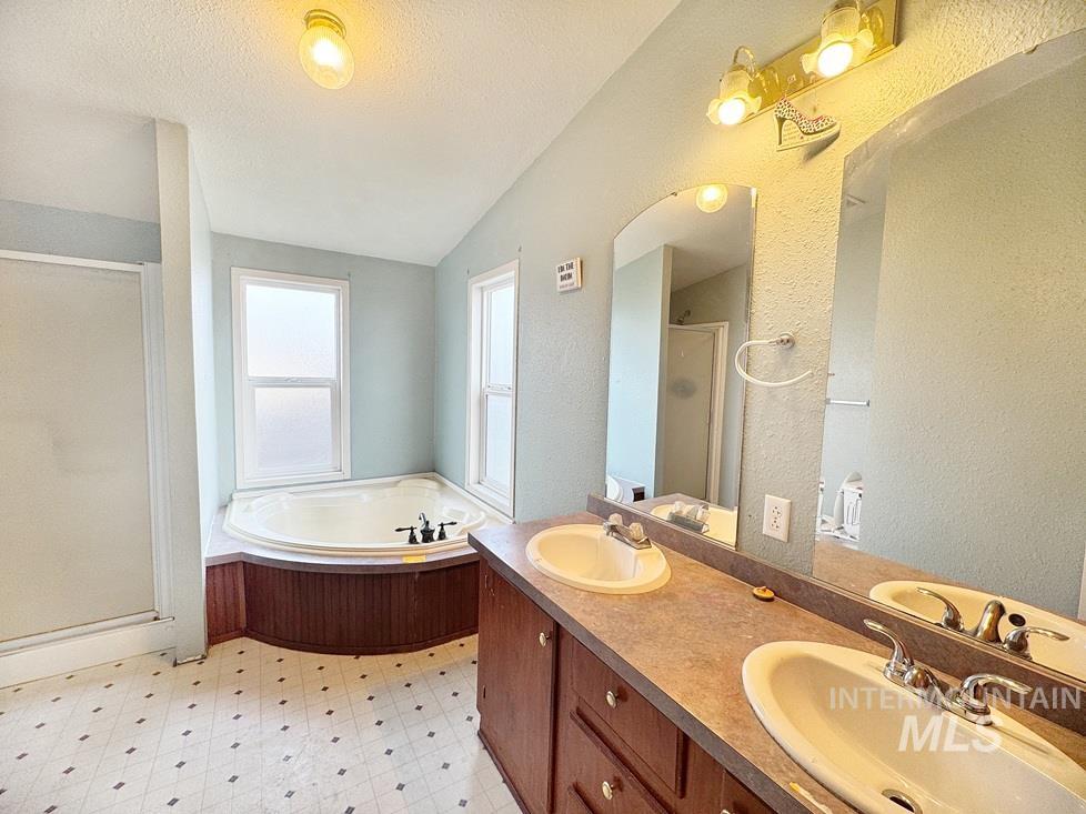 Full bath with a shower stall, a garden tub, a textured wall, a textured ceiling, and double vanity