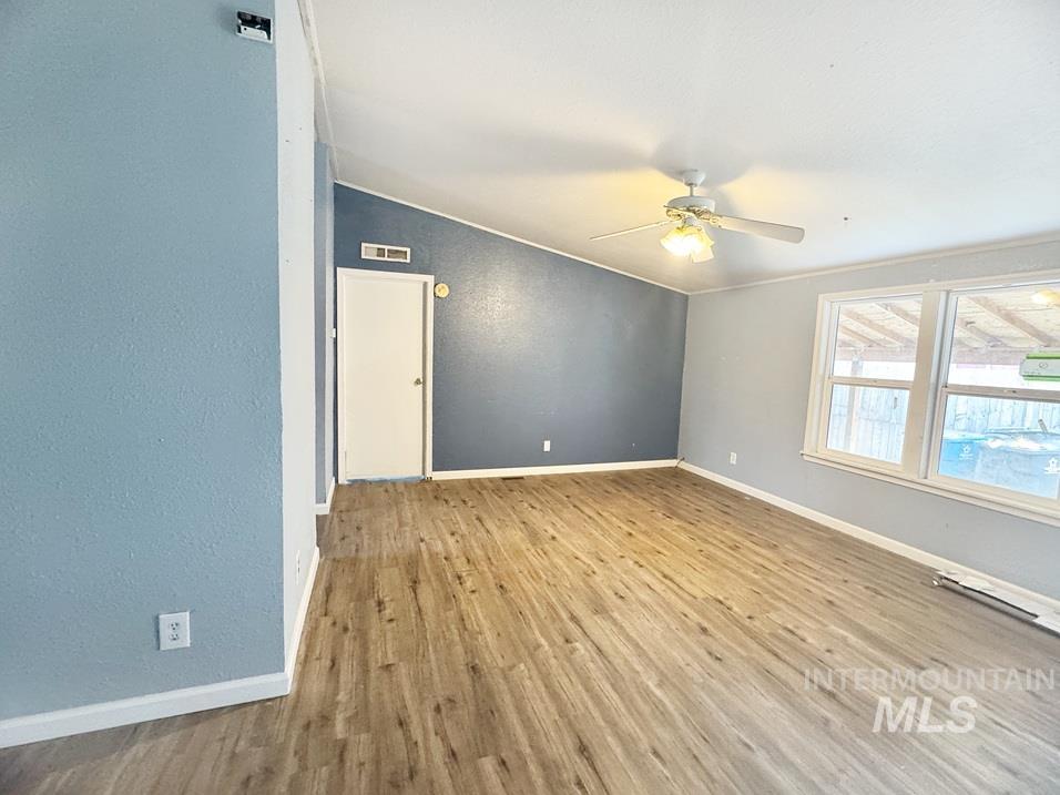 Empty room with vaulted ceiling, light wood-style floors, and ceiling fan