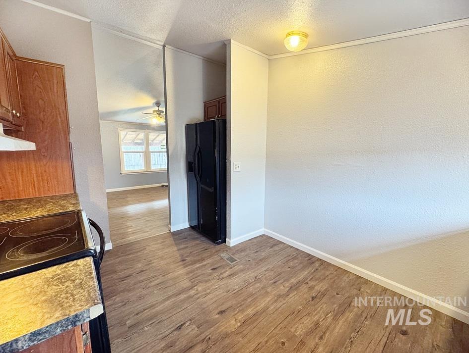 Kitchen with light wood finished floors, a textured ceiling, a textured wall, black fridge, and brown cabinets