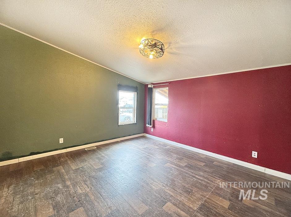Unfurnished room with a textured ceiling, dark wood-type flooring, crown molding, and a textured wall