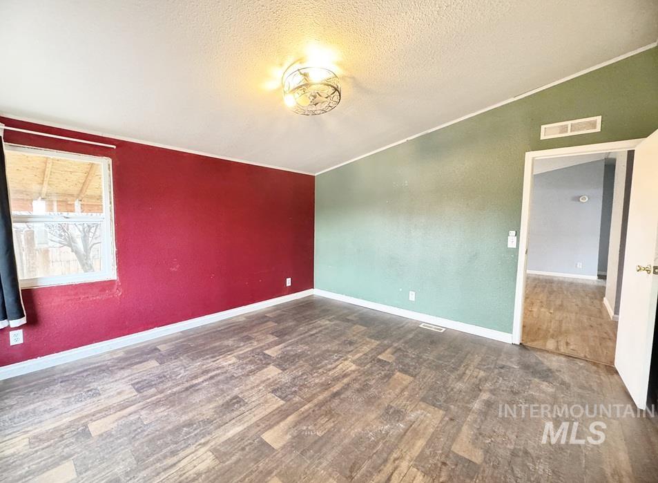 Unfurnished room featuring vaulted ceiling, dark wood-type flooring, and a textured ceiling