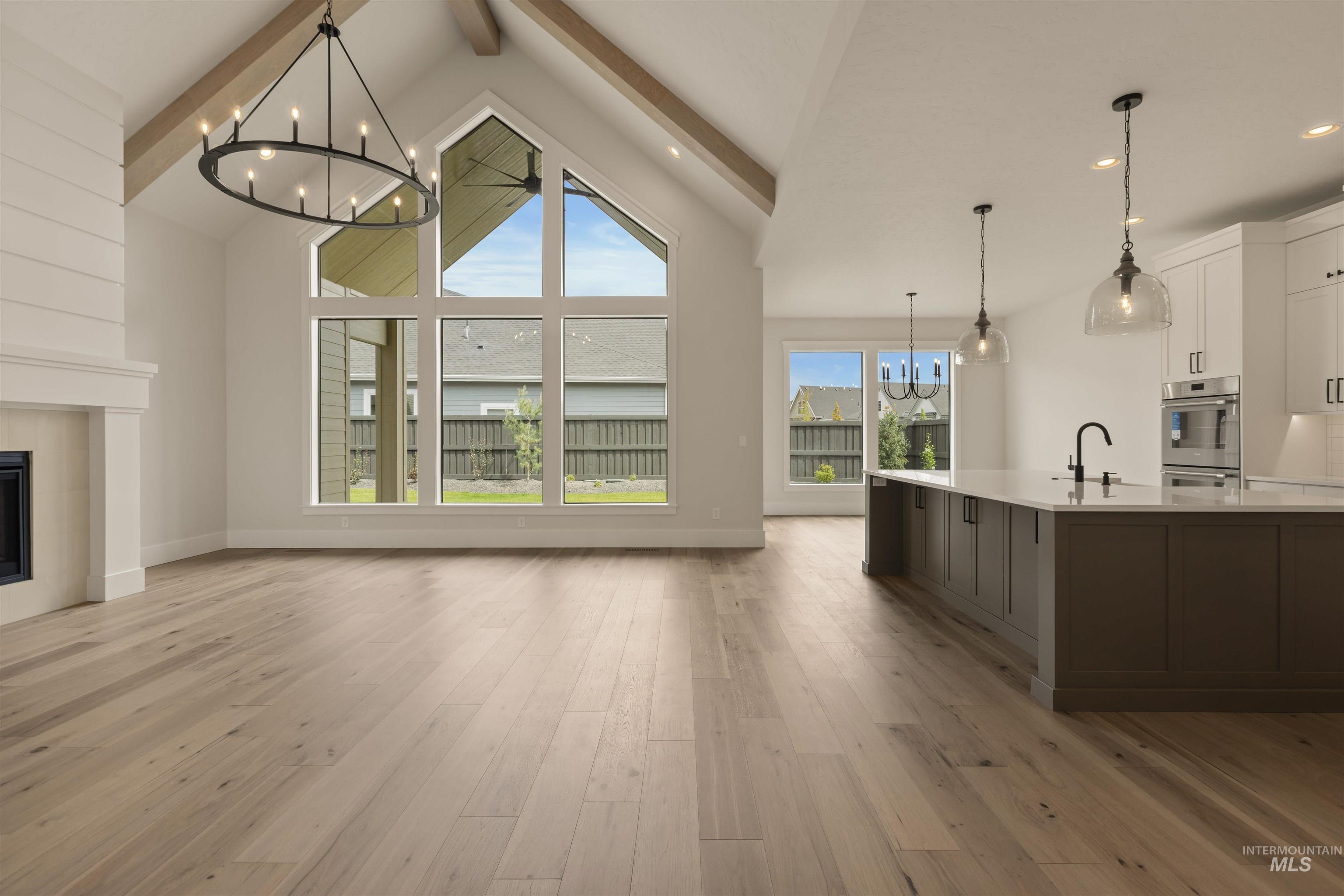 Unfurnished living room with a chandelier, beam ceiling, light wood finished floors, a tiled fireplace, and high vaulted ceiling