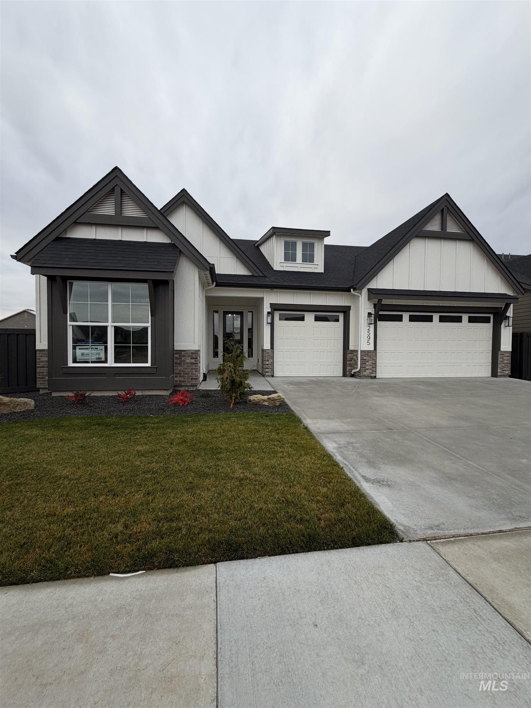View of front of house with concrete driveway, a front lawn, stone siding, board and batten siding, and an attached garage