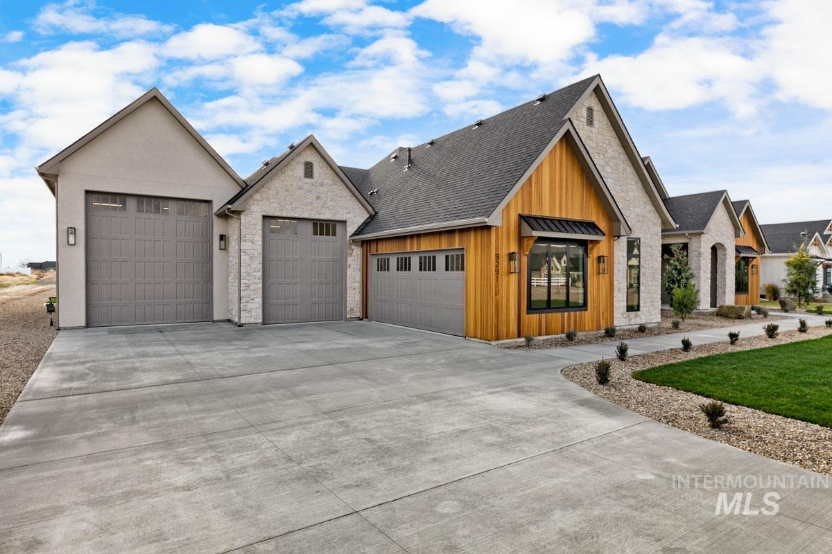View of front of house featuring board and batten siding, driveway, an attached garage, roof with shingles, and stone siding