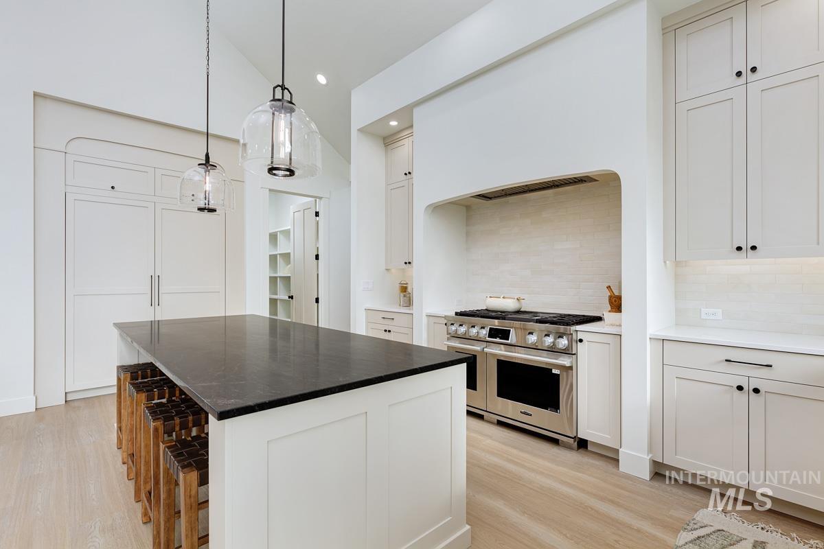 Kitchen featuring white cabinetry, a breakfast bar area, range with two ovens, pendant lighting, and a center island