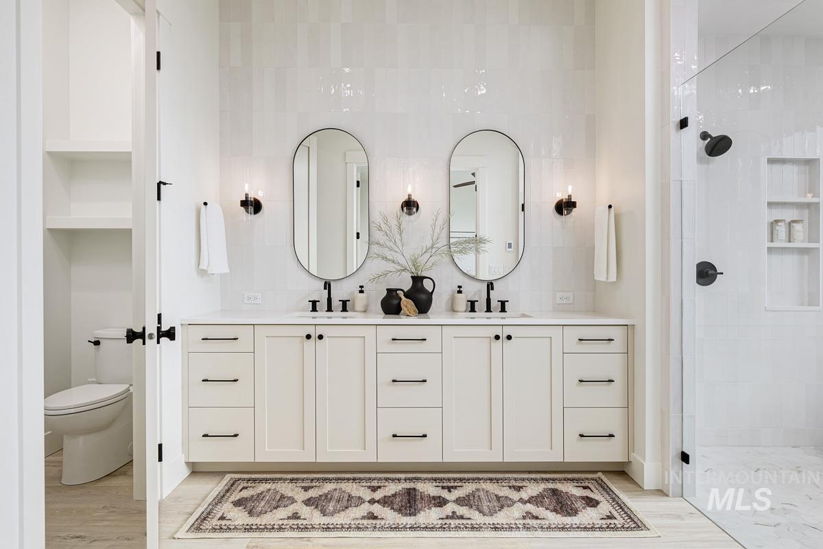 Bathroom with double vanity, tiled shower, and light wood-style floors