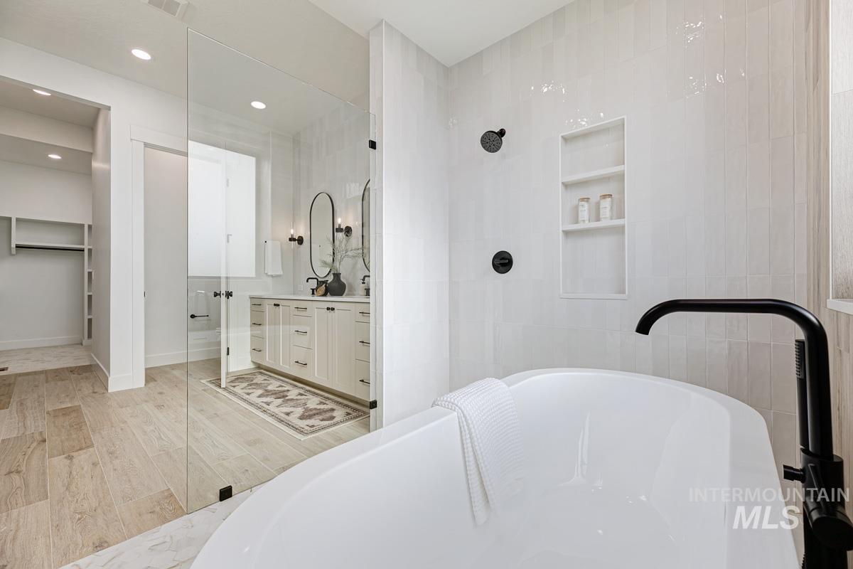 Bathroom with vanity, a freestanding tub, tile walls, a shower with door, and light wood-style flooring