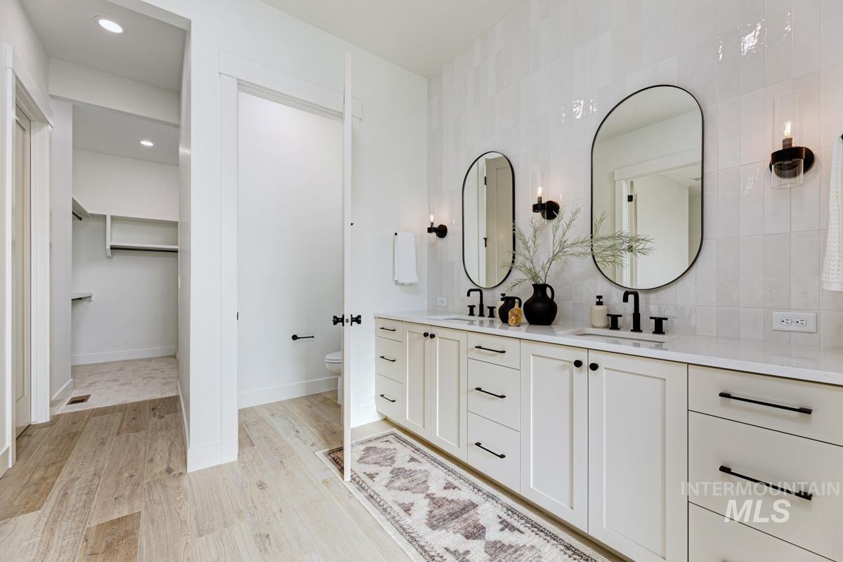 Bathroom with double vanity, a spacious closet, light wood-style floors, decorative backsplash, and recessed lighting