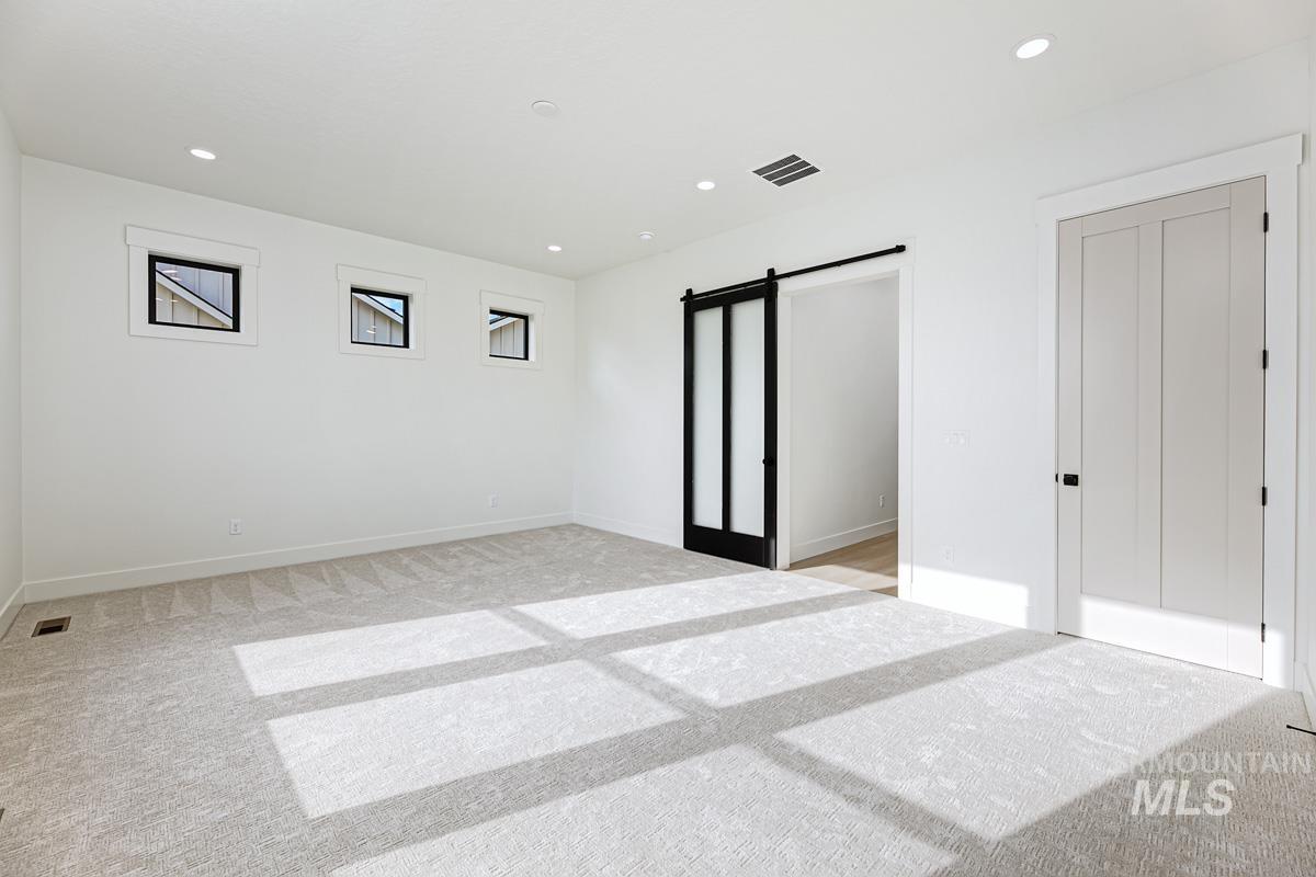 Unfurnished bedroom with a barn door, recessed lighting, and light carpet
