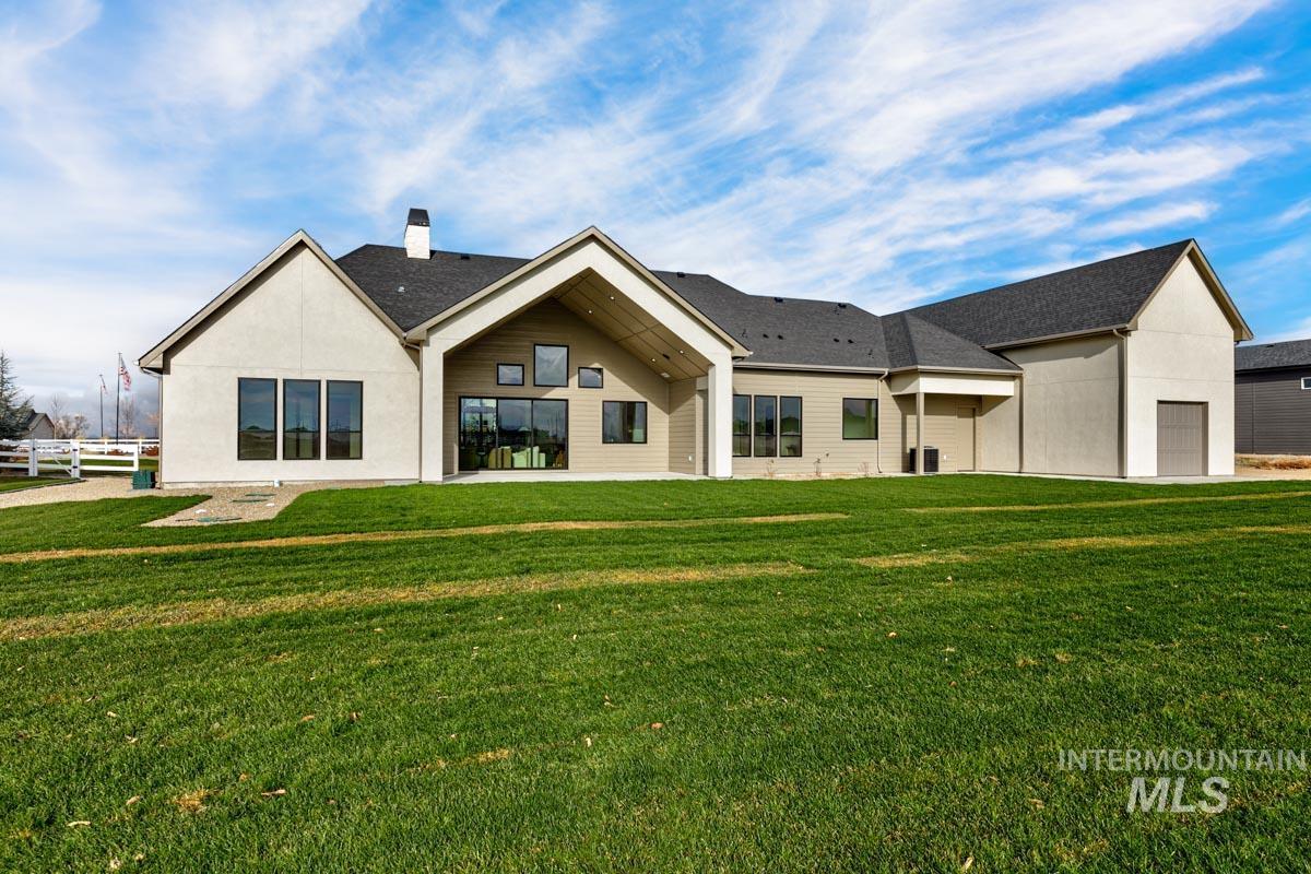 Rear view of property featuring a lawn, a patio, a chimney, a shingled roof, and stucco siding