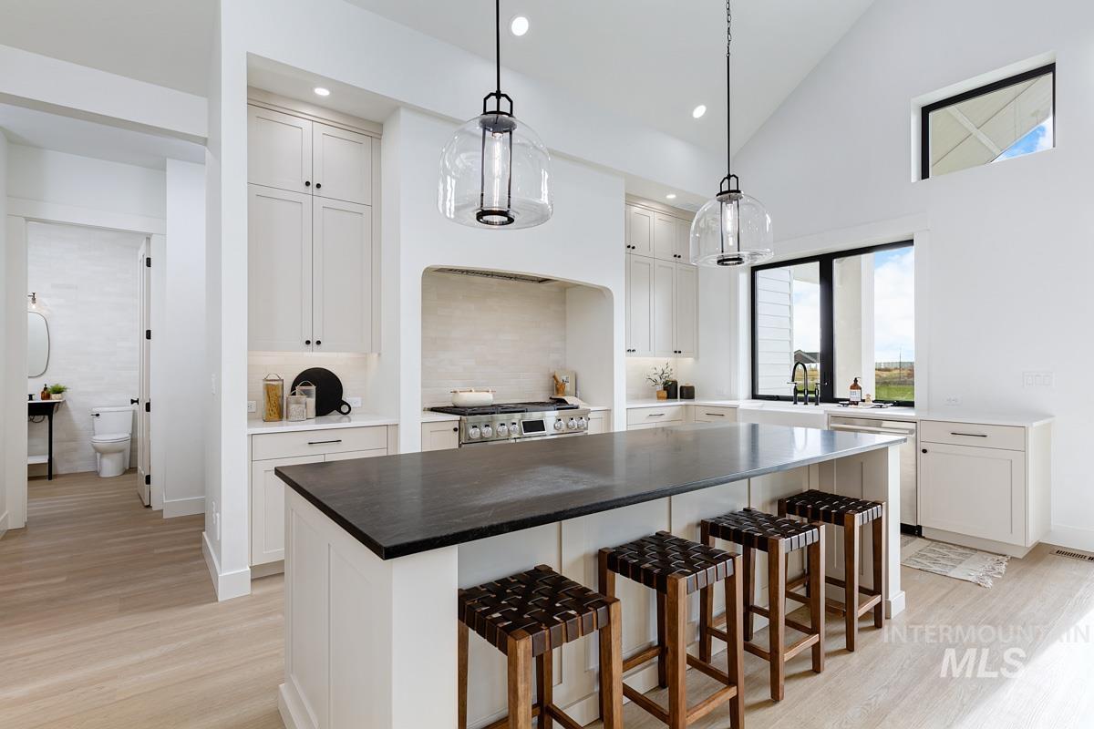 Kitchen with a kitchen bar, decorative light fixtures, a kitchen island, high vaulted ceiling, and light wood-style floors