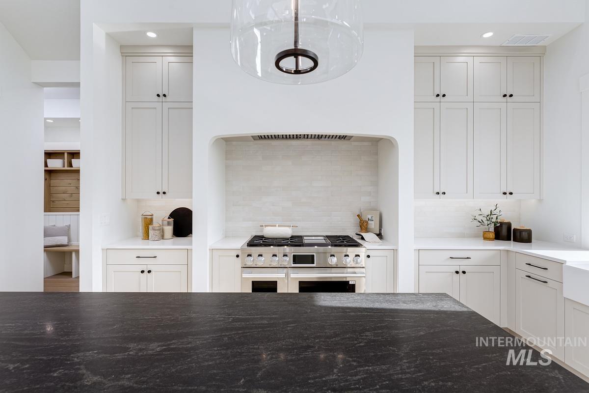 Kitchen featuring dark stone counters, range with two ovens, recessed lighting, decorative backsplash, and white cabinets