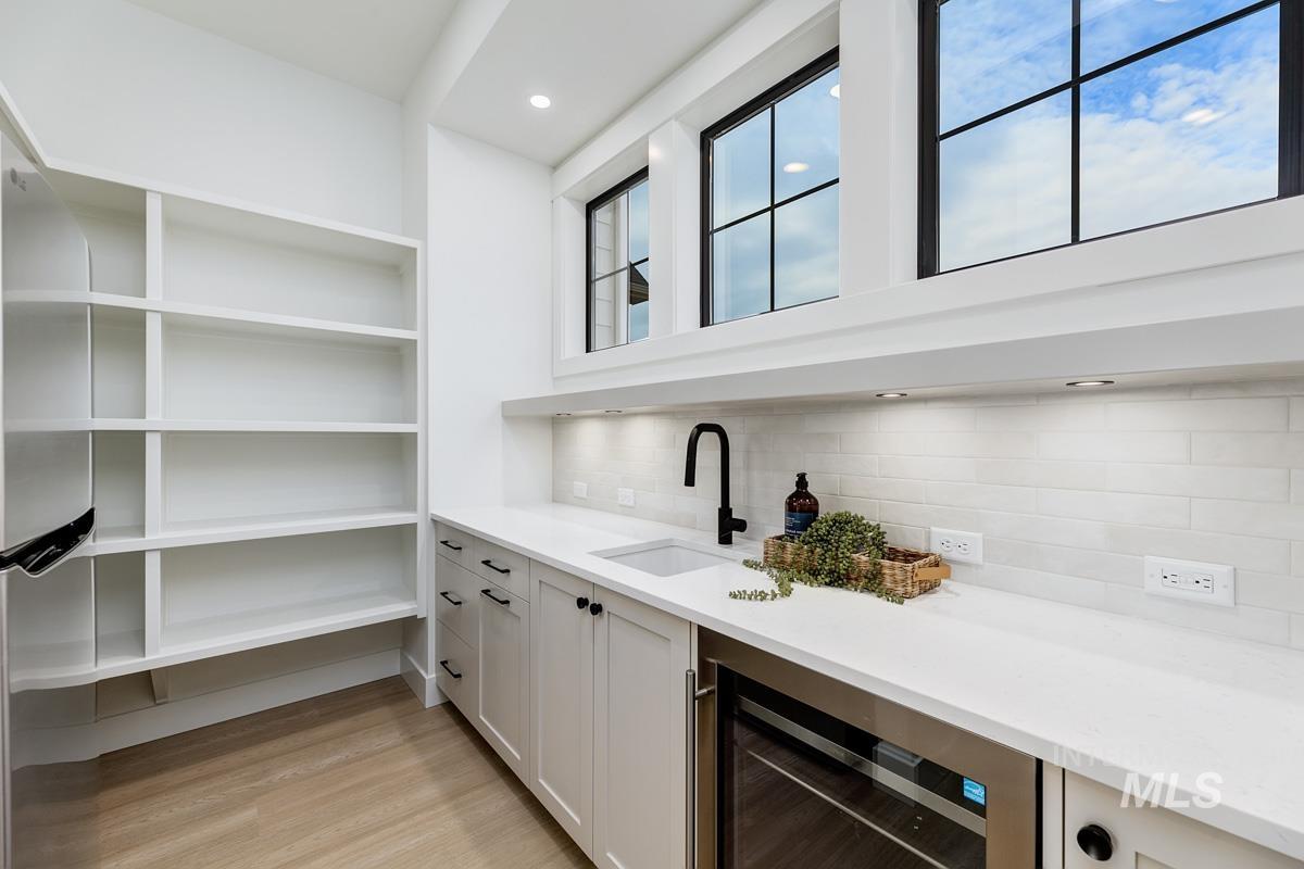 Bar area with wine cooler, light wood-style floors, light stone countertops, tasteful backsplash, and freestanding refrigerator