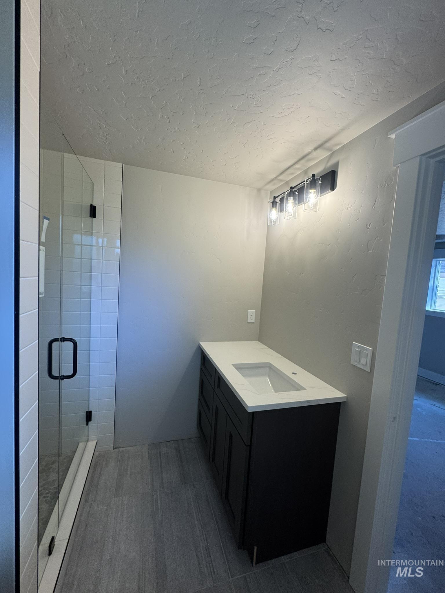 Full bathroom with vanity, a shower stall, and a textured ceiling