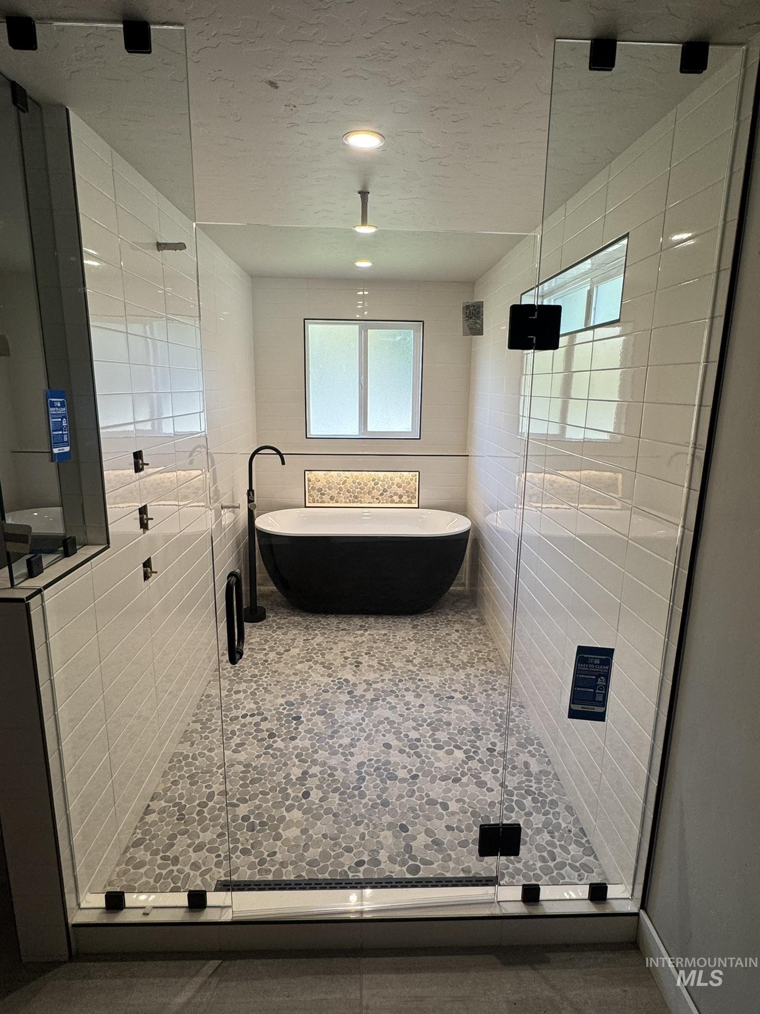 Bathroom with a soaking tub, a textured ceiling, tile walls, and a shower stall