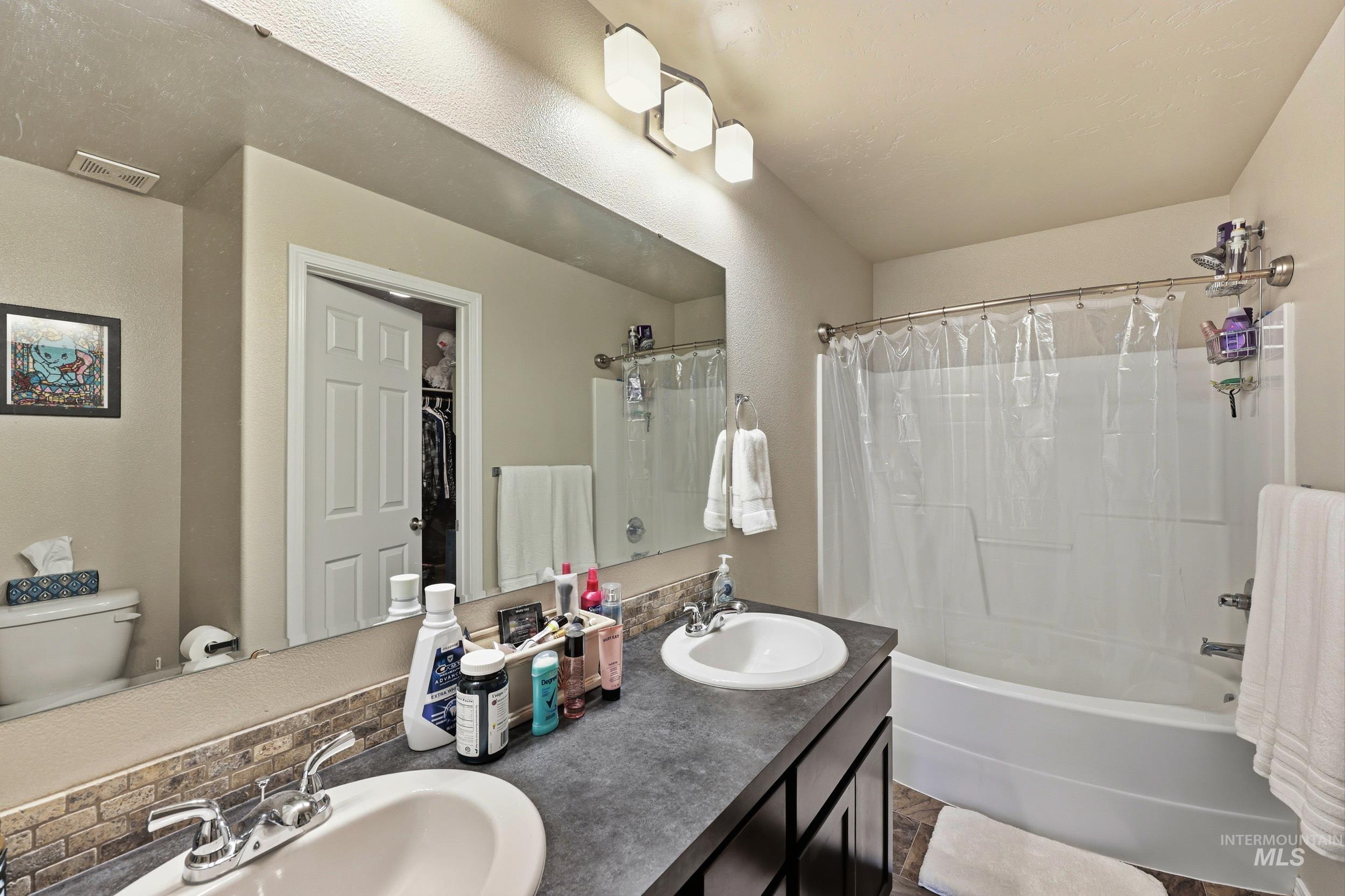 Full bath featuring double vanity, shower / bath combo, and a spacious closet