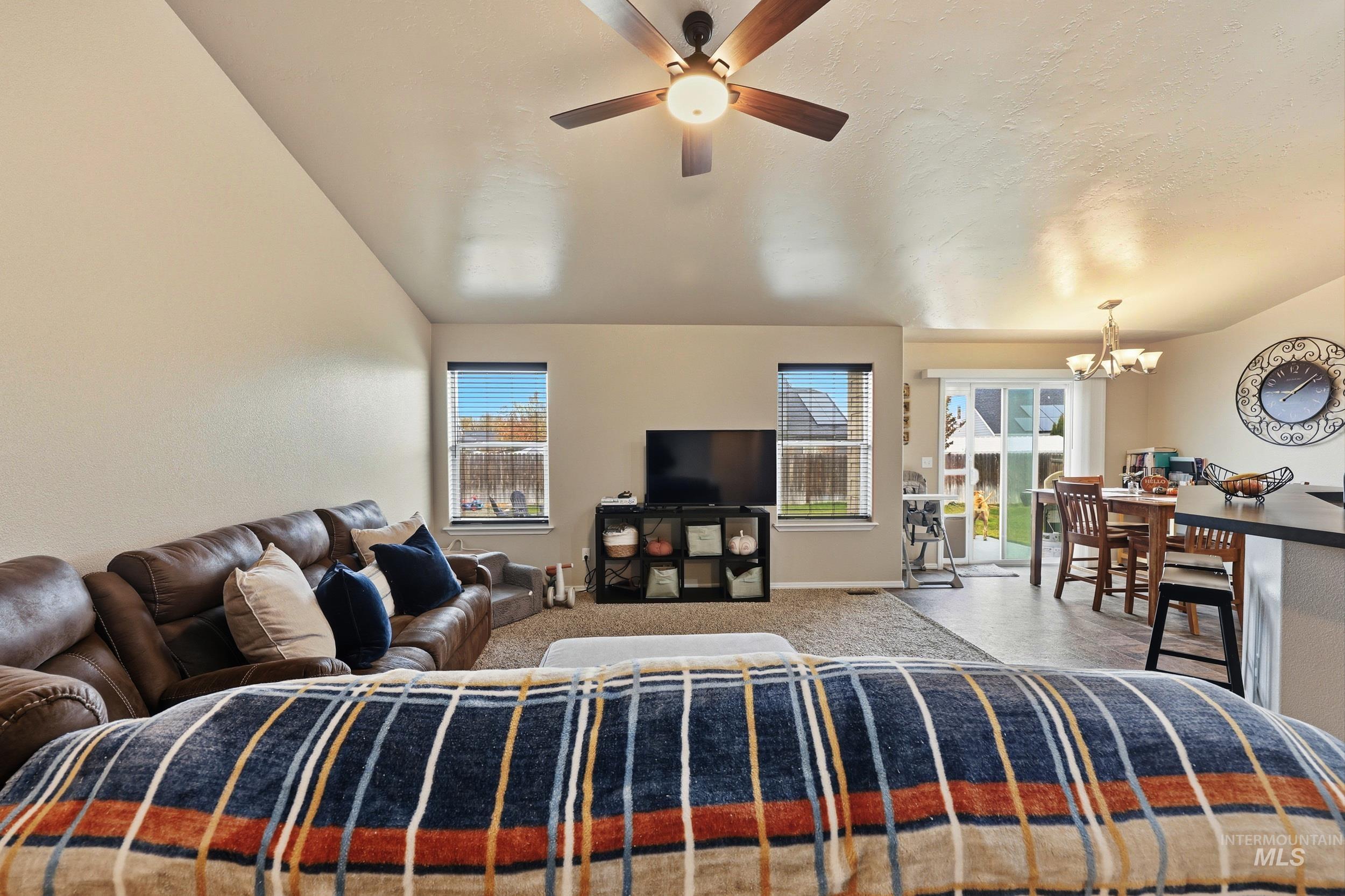 Living room featuring plenty of natural light, lofted ceiling, a ceiling fan, a chandelier, and carpet flooring