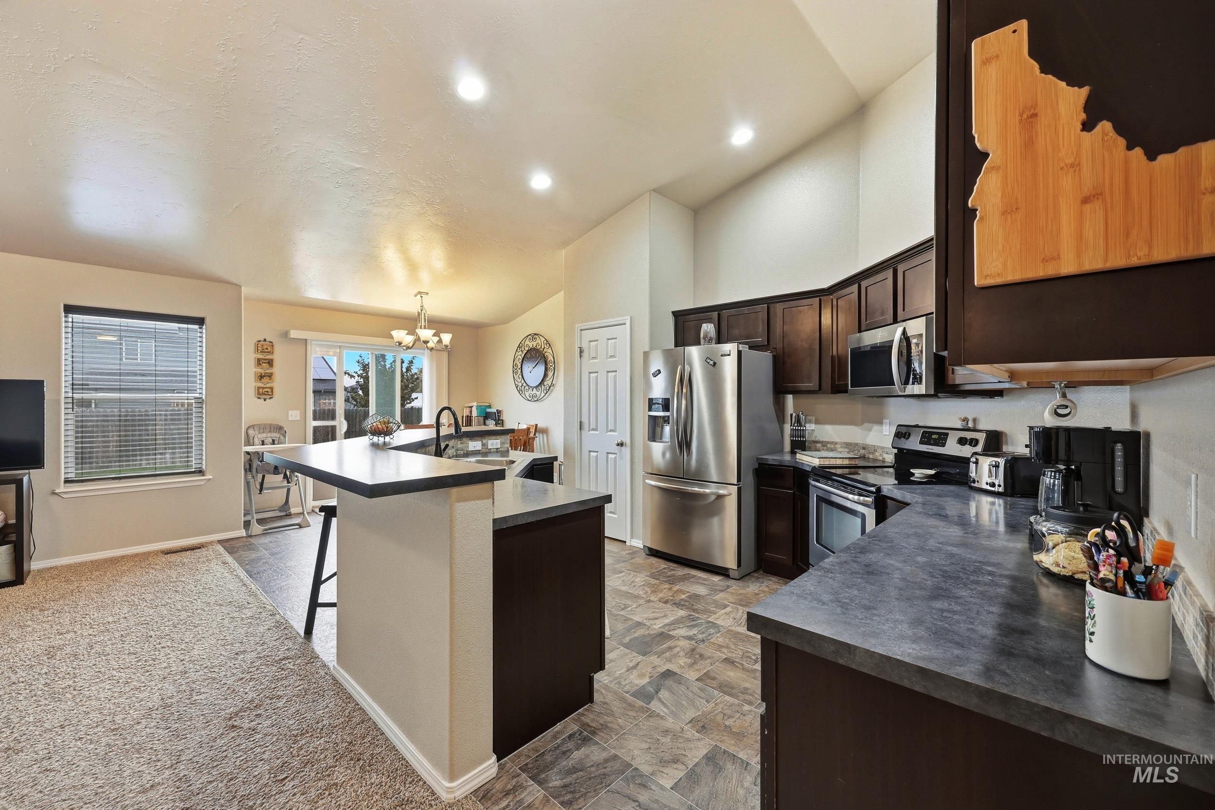 Kitchen featuring dark brown cabinetry, a kitchen breakfast bar, a chandelier, appliances with stainless steel finishes, and dark countertops