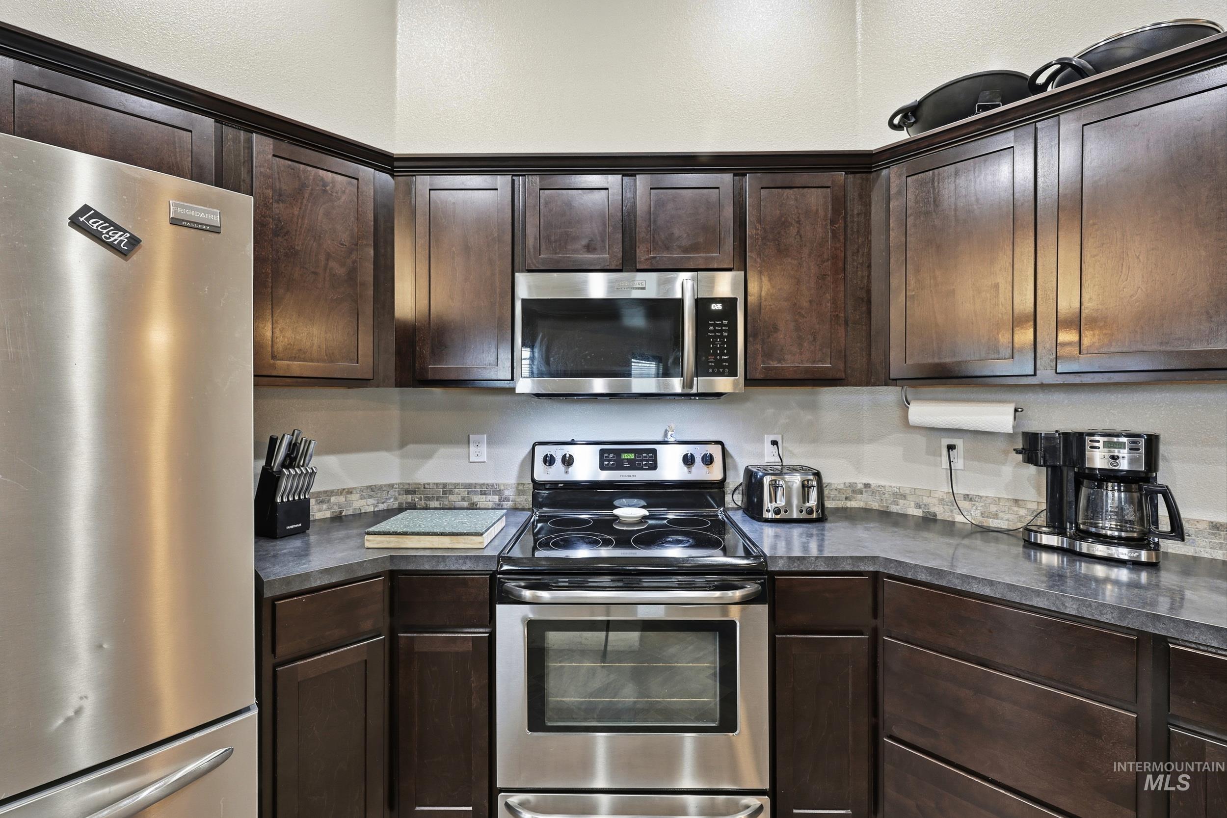 Kitchen featuring stainless steel appliances, dark brown cabinets, and dark countertops