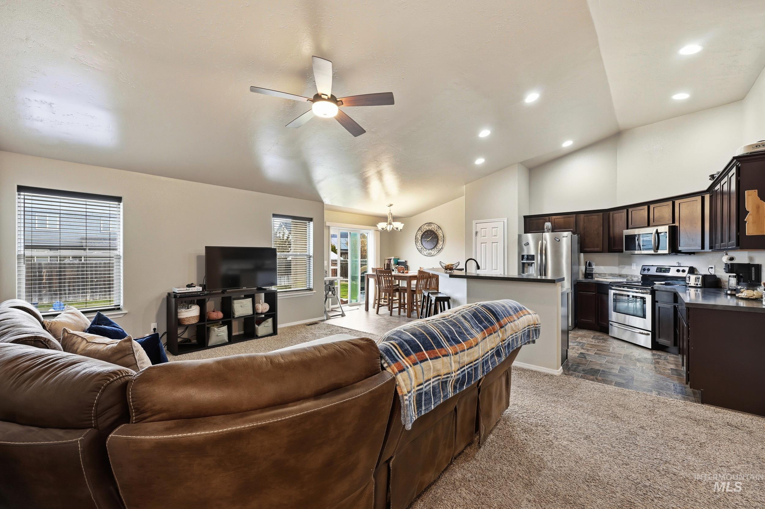 Living area featuring lofted ceiling, a chandelier, a ceiling fan, dark colored carpet, and recessed lighting