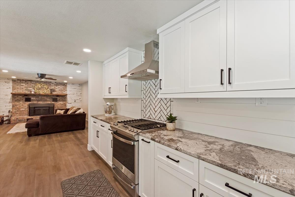 Kitchen with stainless steel range with gas stovetop, white cabinetry, wall chimney exhaust hood, light stone counters, and recessed lighting