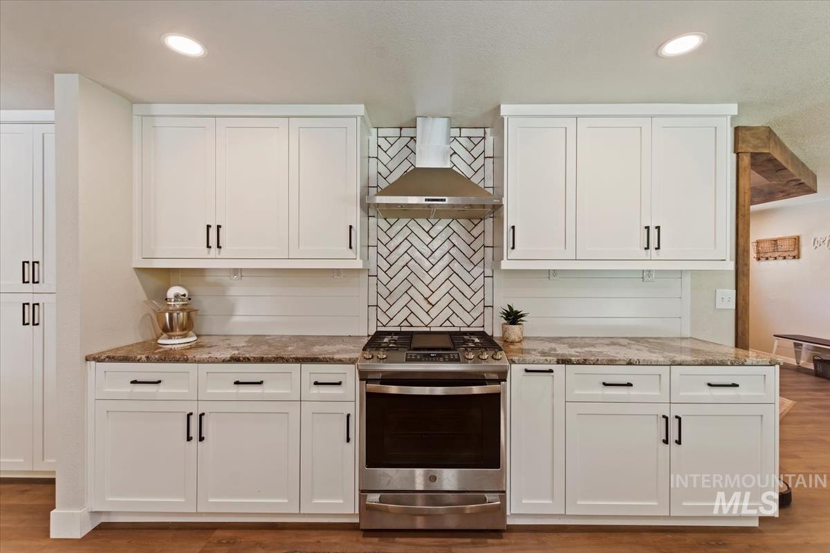 Kitchen with gas range, white cabinetry, light stone countertops, light wood-style floors, and recessed lighting