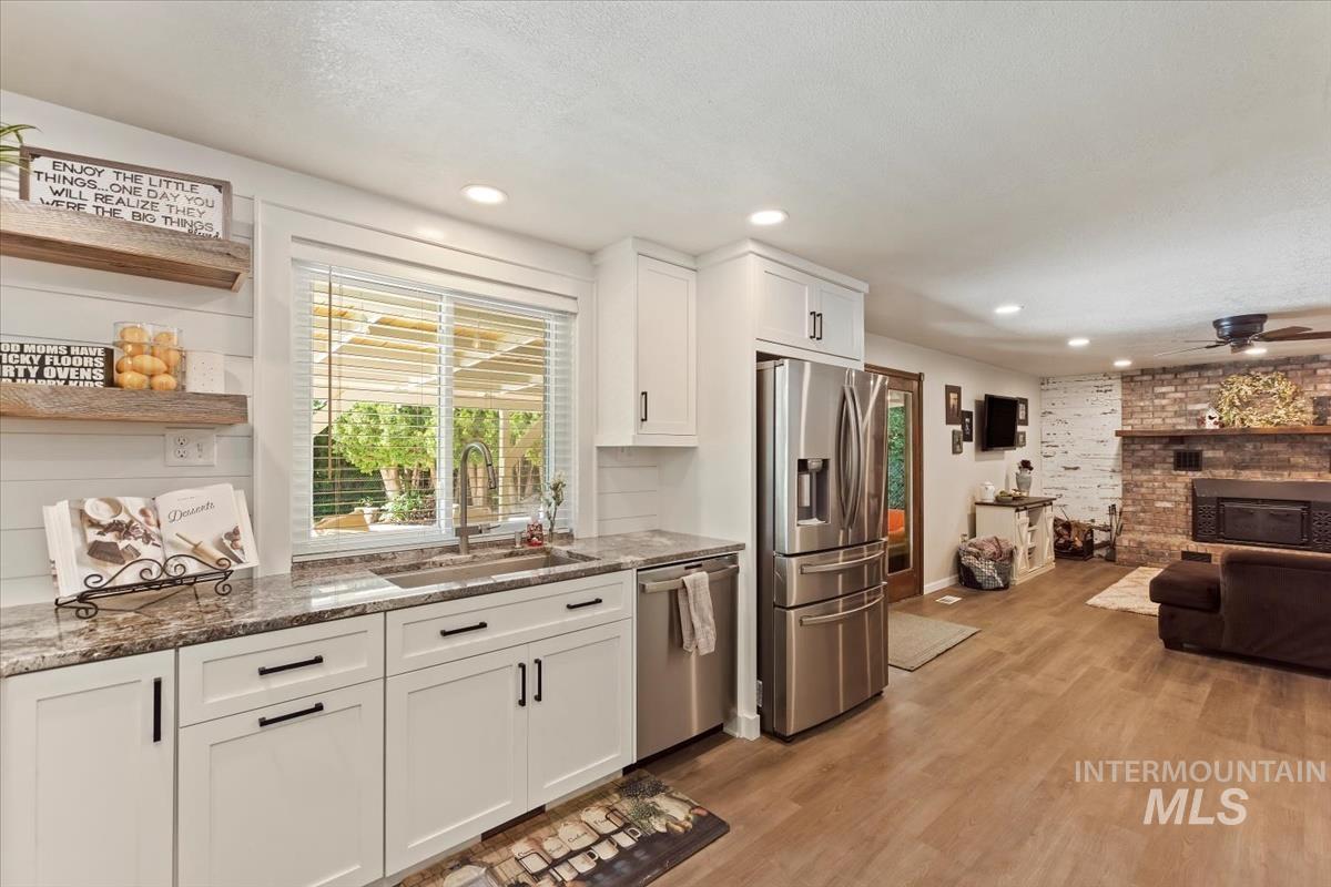 Kitchen featuring stainless steel appliances, white cabinetry, a ceiling fan, dark stone counters, and light wood-style flooring
