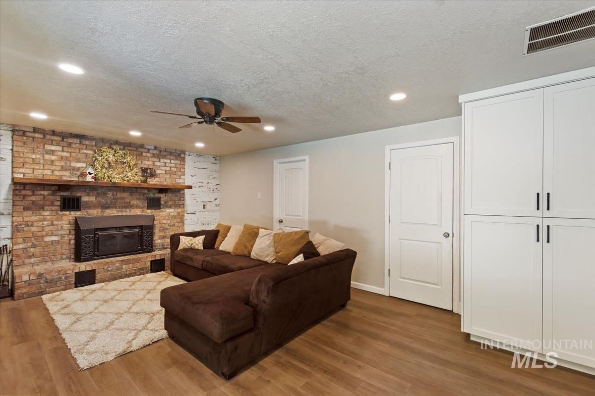 Living area with a textured ceiling, wood finished floors, recessed lighting, a ceiling fan, and a brick fireplace