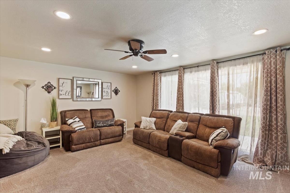 Carpeted living room with a textured ceiling, ceiling fan, and recessed lighting