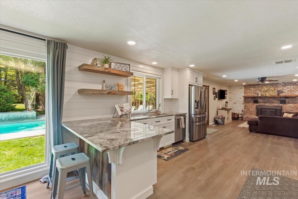 Kitchen with a breakfast bar area, open shelves, light stone countertops, stainless steel appliances, and light wood-style flooring