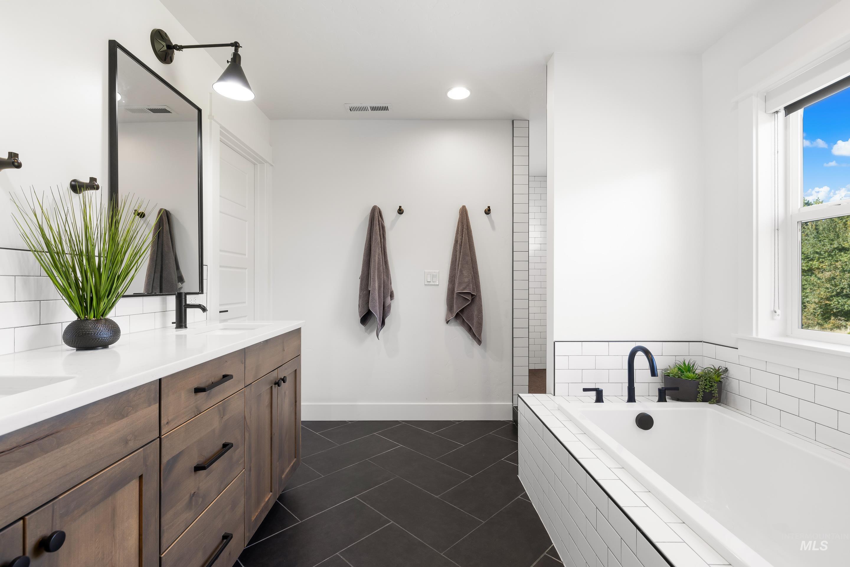 Full bathroom with a garden tub, double vanity, dark tile patterned floors, and recessed lighting